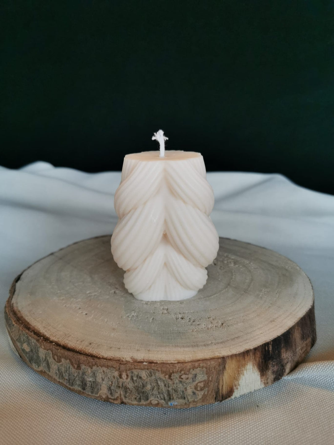 Handgegossene Kerze aus cremefarbenem Rapswachs in Tannenform, fotografiert auf einer Holzscheibe.