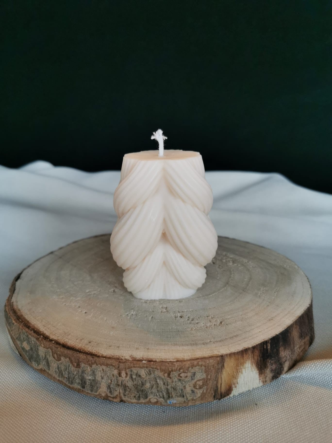 Handgegossene Kerze aus cremefarbenem Rapswachs in Tannenform, fotografiert auf einer Holzscheibe.