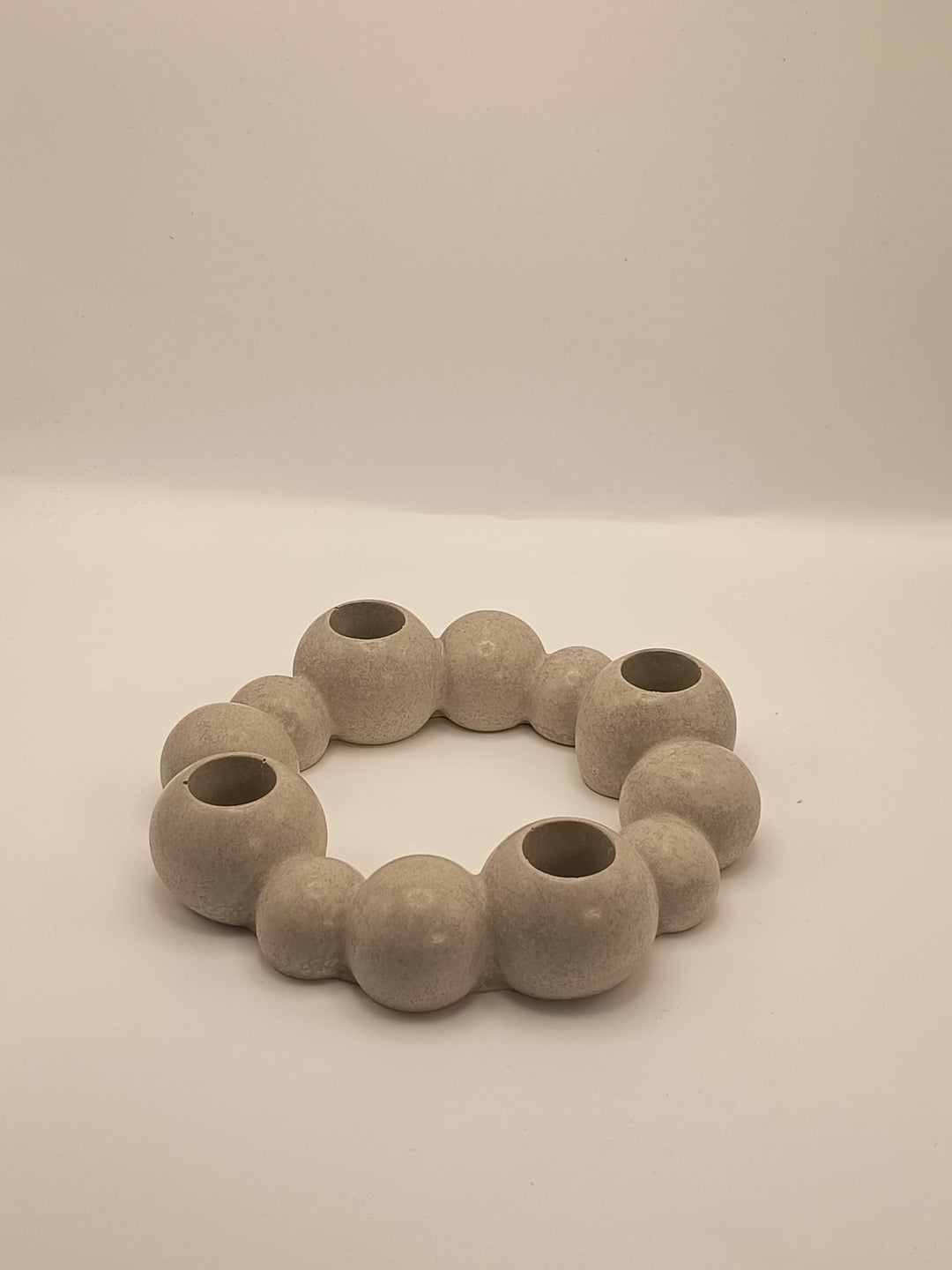 Runder, moderner Kerzenhalter aus Beton in organischer Kugelform, mit vier integrierten Öffnungen für Stabkerzen, auf hellem Hintergrund fotografiert