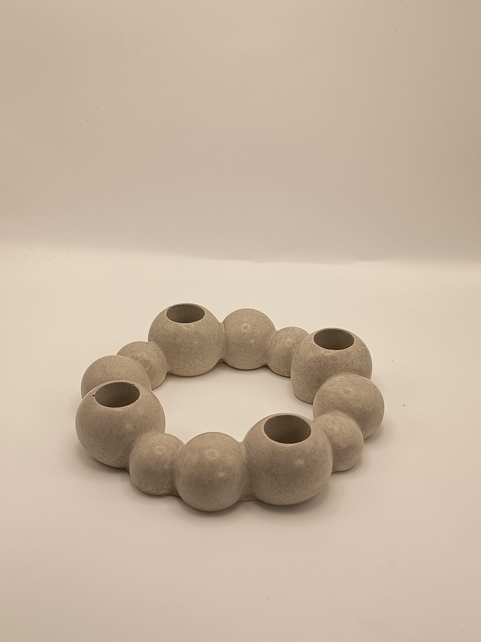 Runder, moderner Kerzenhalter aus Beton in organischer Kugelform, mit vier integrierten Öffnungen für Stabkerzen, auf hellem Hintergrund fotografiert