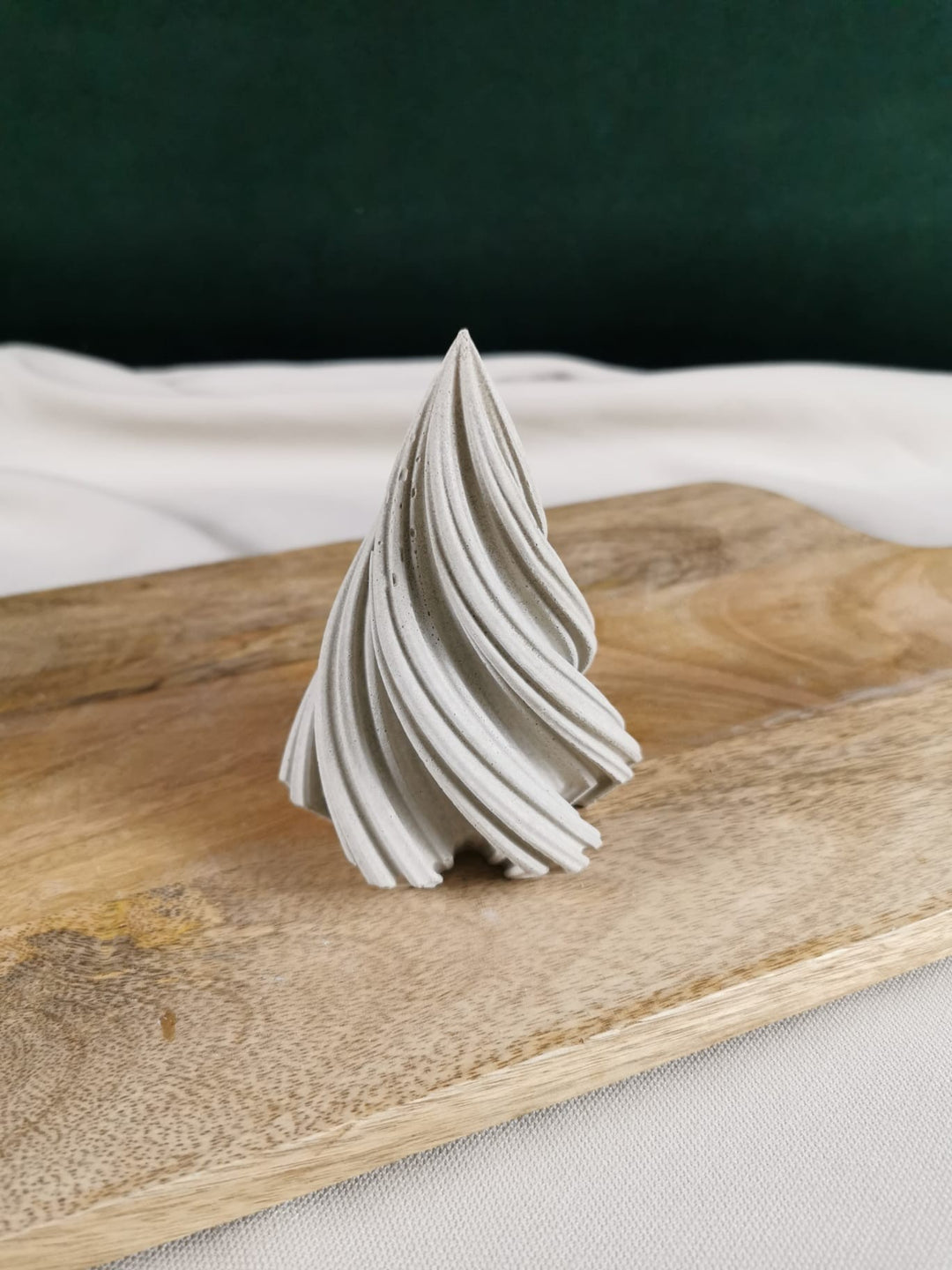 „Handgefertigter geschwungener Beton-Tannenbaum als minimalistische Weihnachts- und Winterdekoration auf Holzbrett.“