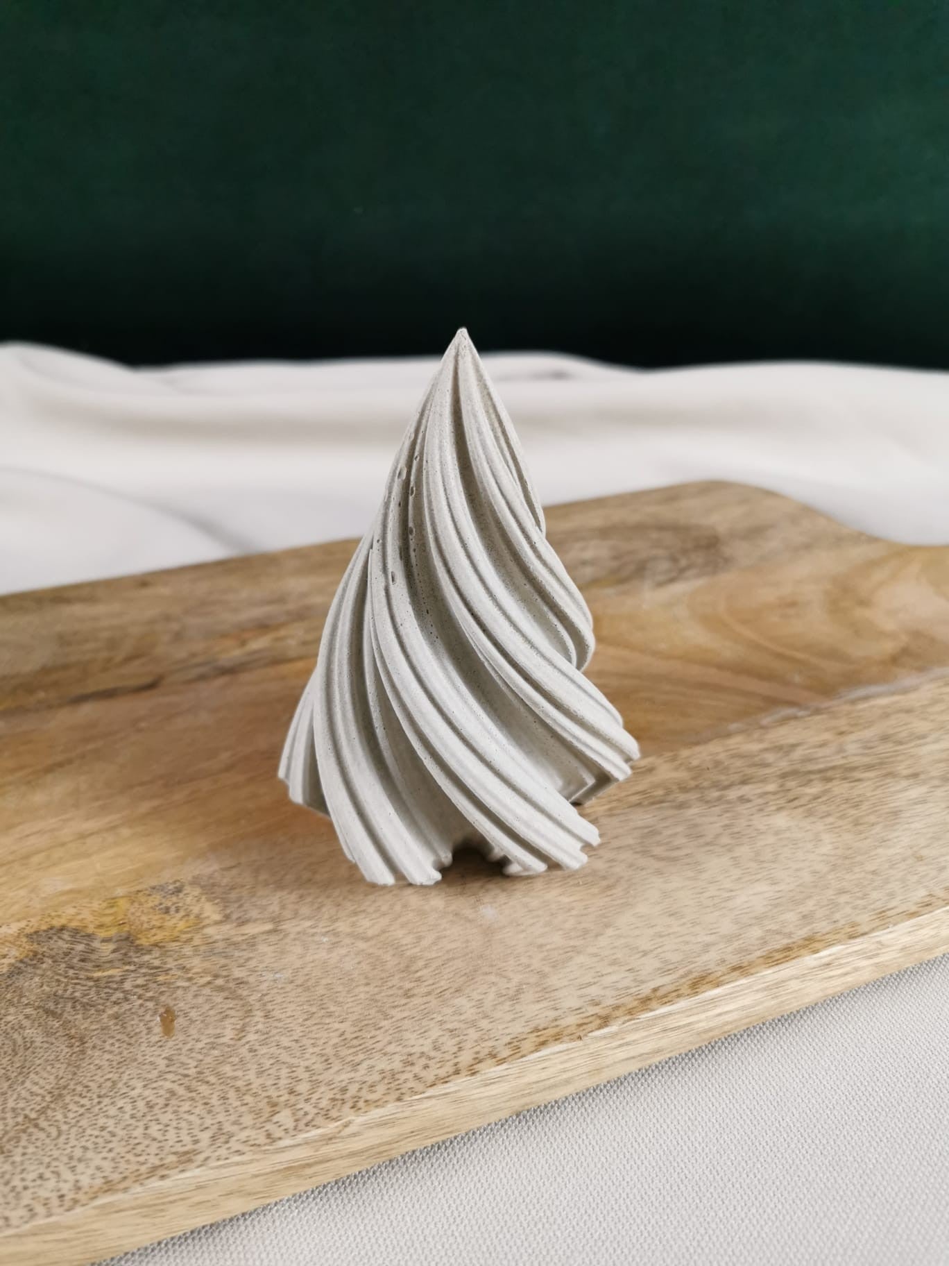 „Handgefertigter geschwungener Beton-Tannenbaum als minimalistische Weihnachts- und Winterdekoration auf Holzbrett.“