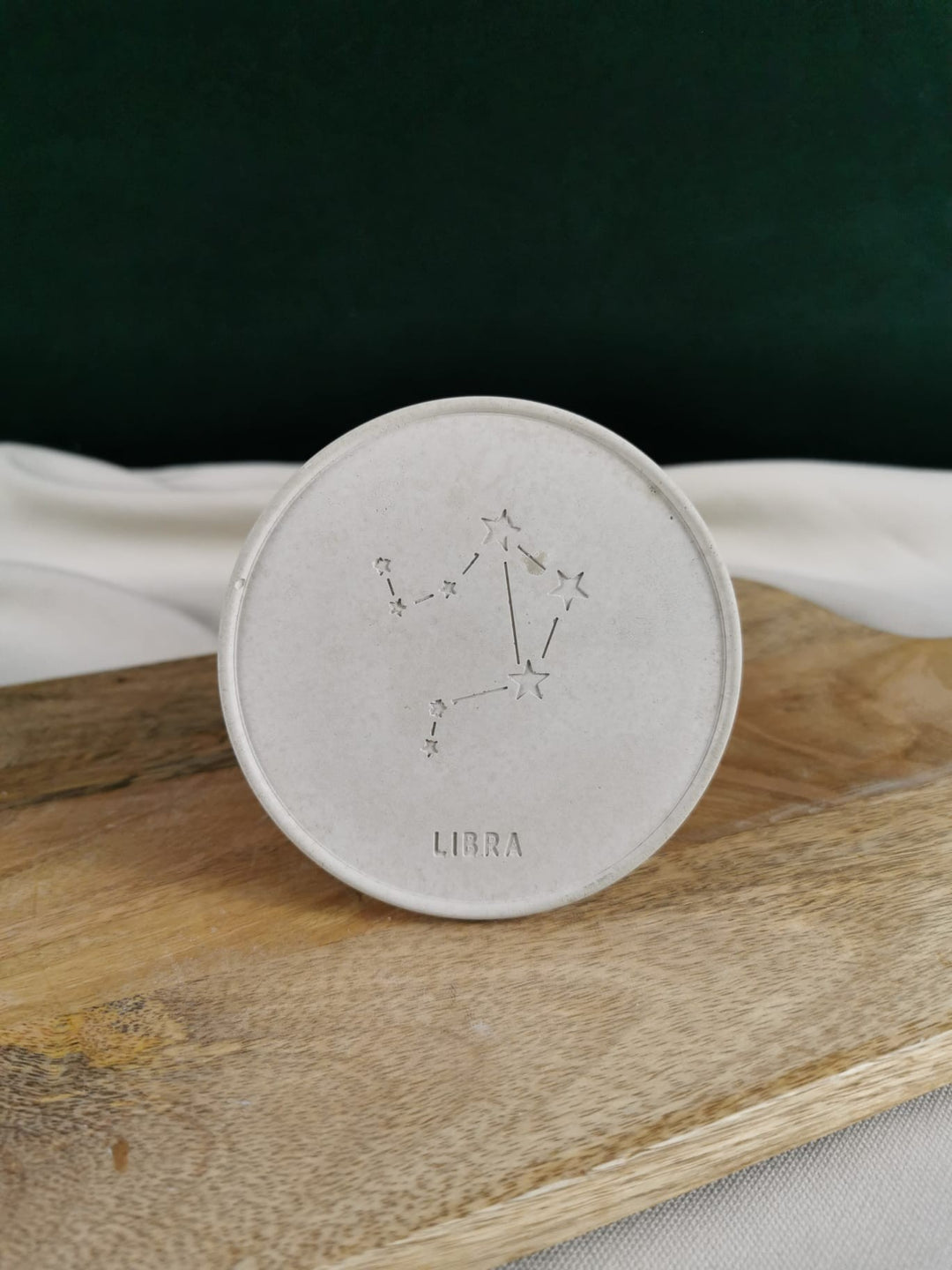 „Handgefertigter runder Beton-Untersetzer mit eingraviertem Sternzeichen Libra/Waage und Sternbild, auf Holzunterlage fotografiert“