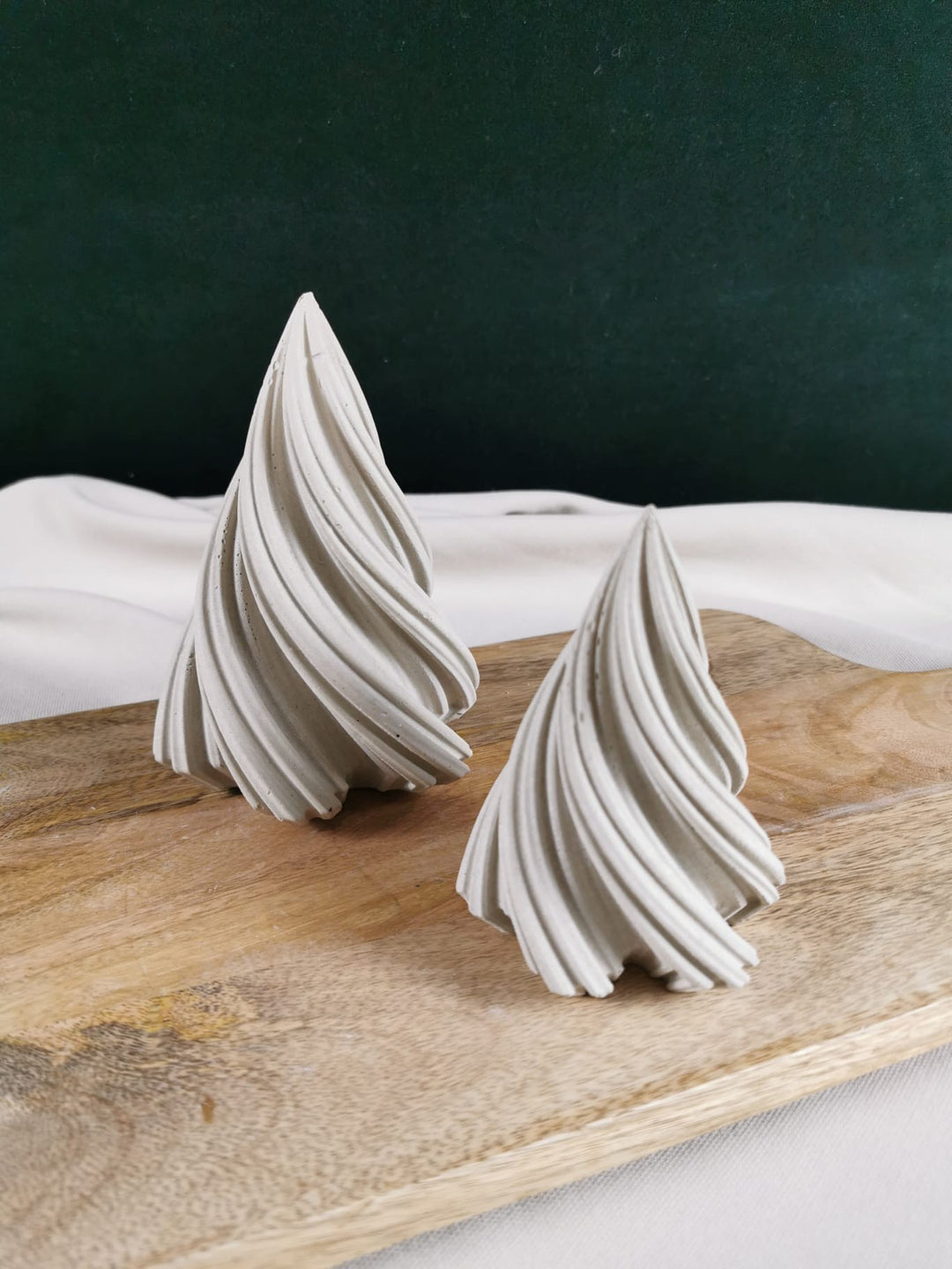 „Zwei handgegossene, geschwungene Weihnachtsbäume aus Beton als stilvolle Winter- und Weihnachtsdekoration auf Holzplatte.“