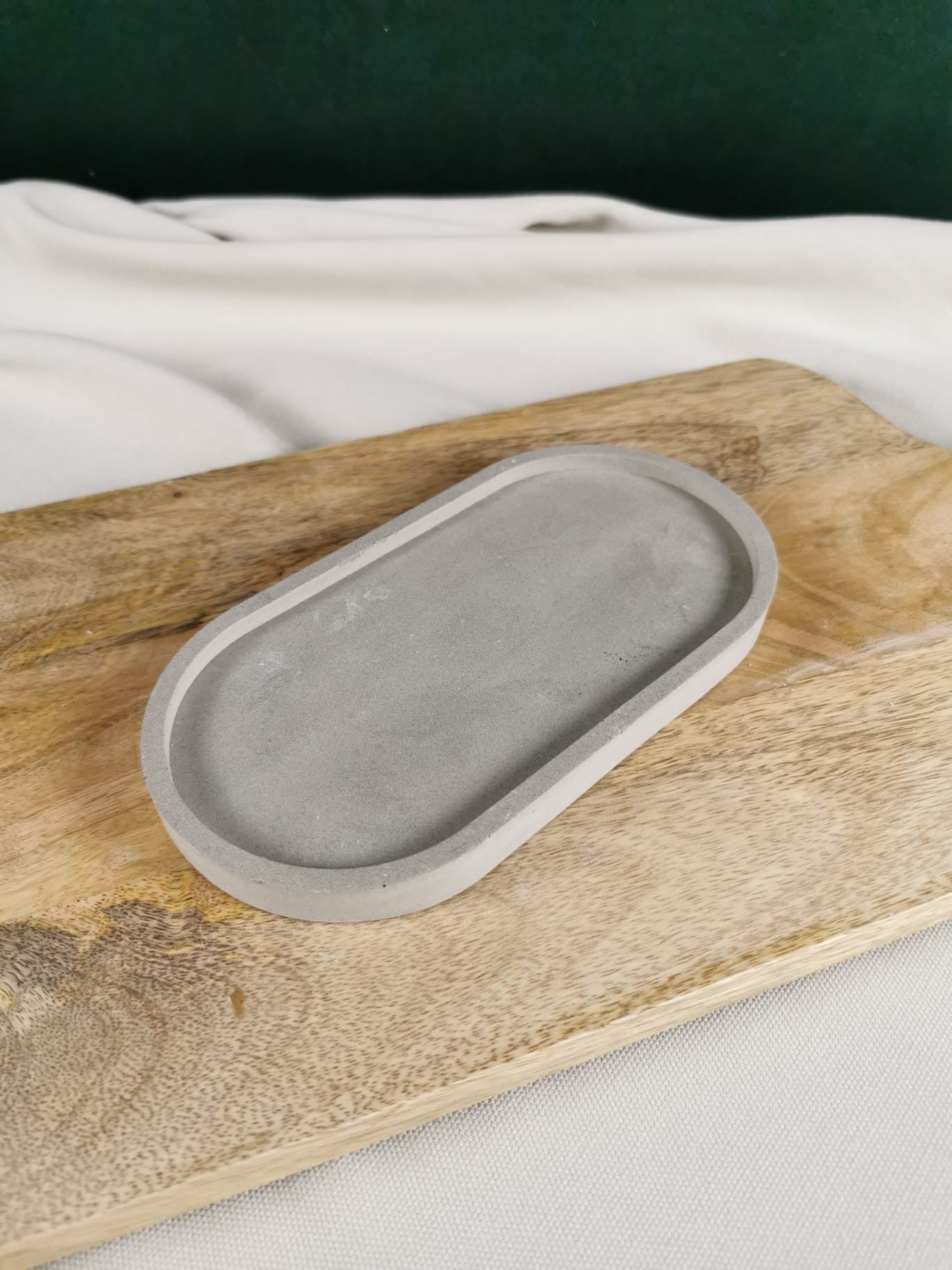 Handgemachte minimalistische Betonablage in ovaler Form, dekorativ auf einem Holzbrett präsentiert, perfekt als Tablett oder Untersetzer.