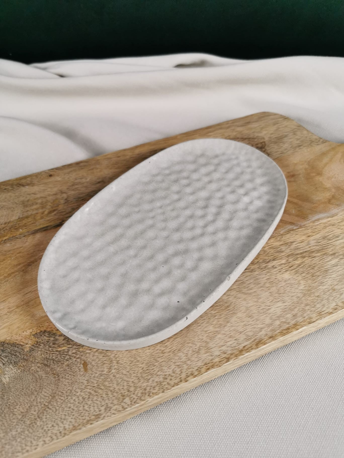 „Handgefertigte ovale Betonschale mit gehämmerter Struktur auf Holzuntergrund – minimalistische Deko in hellem Beton.“