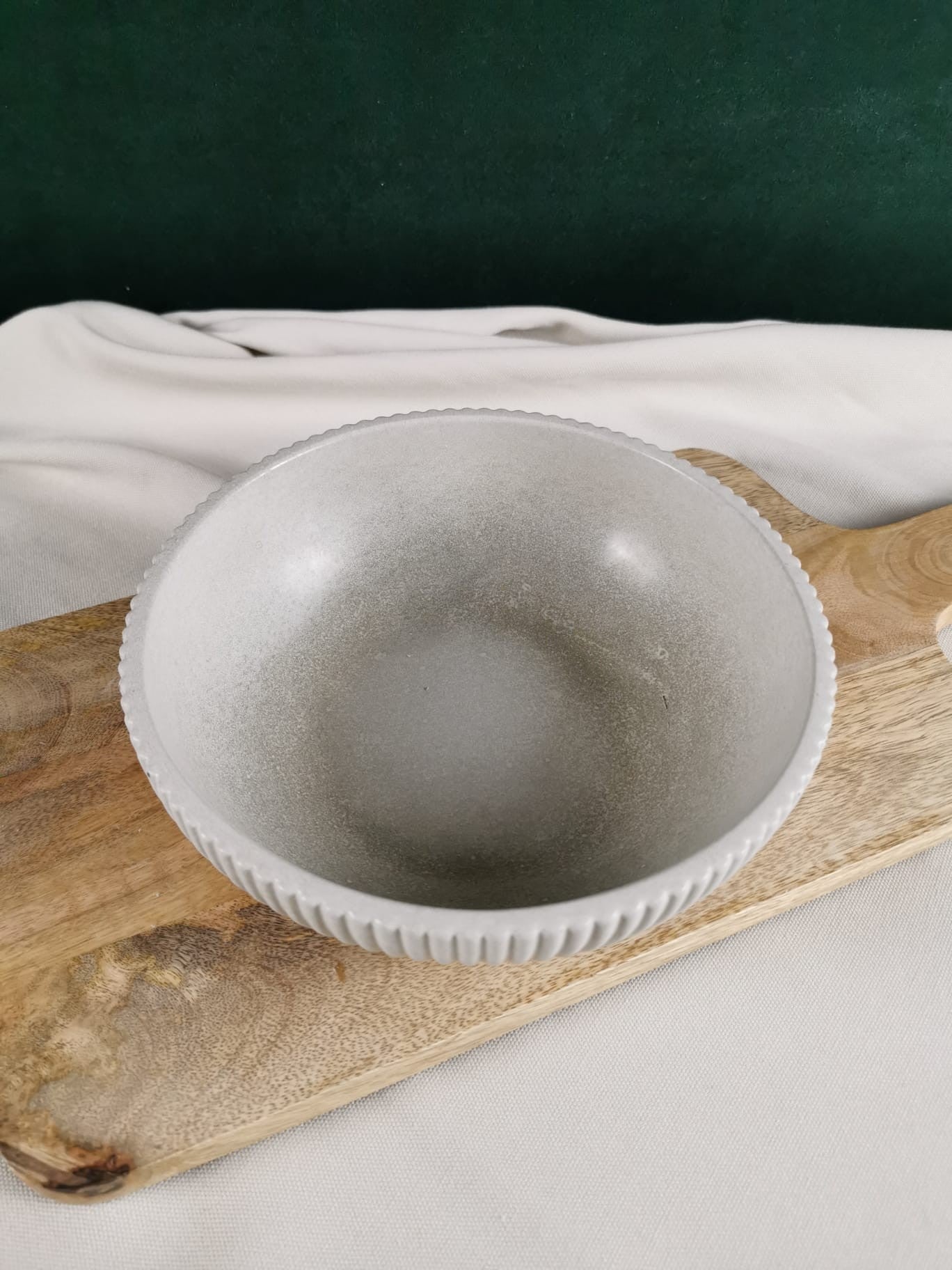 Handgefertigte helle Betonschale mit feiner Rillenstruktur am Rand, dekorativ auf einem Holzbrett platziert.