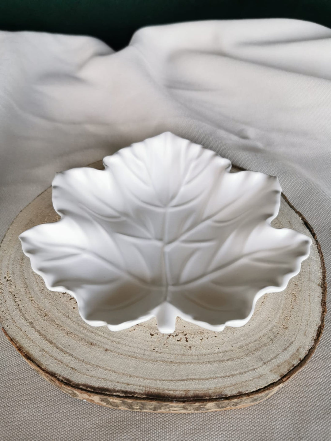 Handgefertigte Blattschale aus weißer Keramik mit feiner Blattstruktur, auf Holzuntergrund platziert – modernes, natürliches Wohnaccessoire