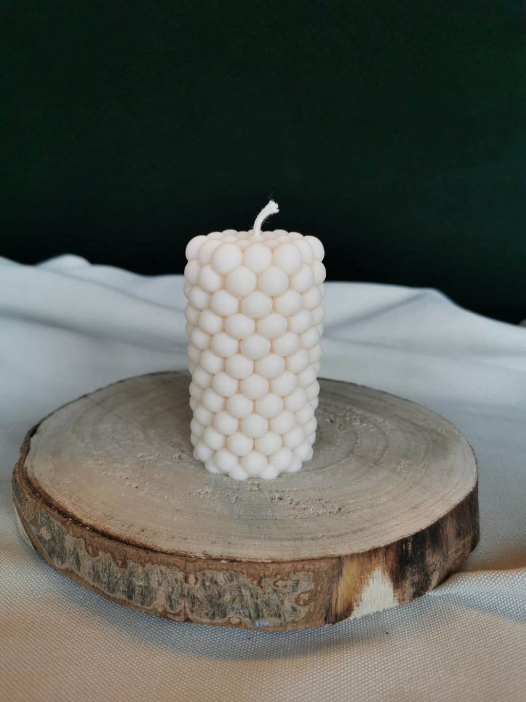 Handgegossene zylindrische Bubble-Kerze aus naturfarbenem Rapswachs, dekorativ auf einer Baumscheibe präsentiert.