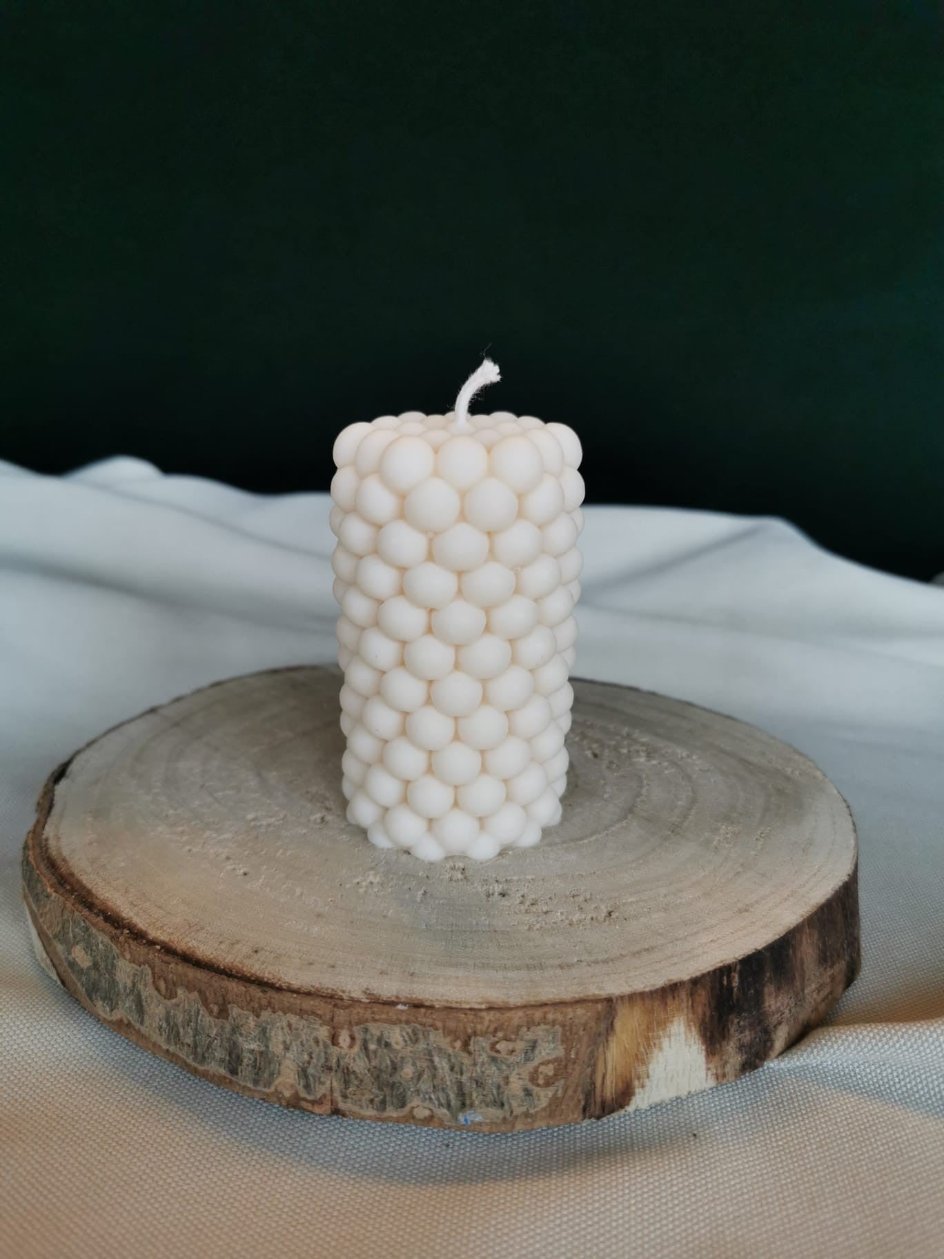 Handgegossene zylindrische Bubble-Kerze aus naturfarbenem Rapswachs, dekorativ auf einer Baumscheibe präsentiert.