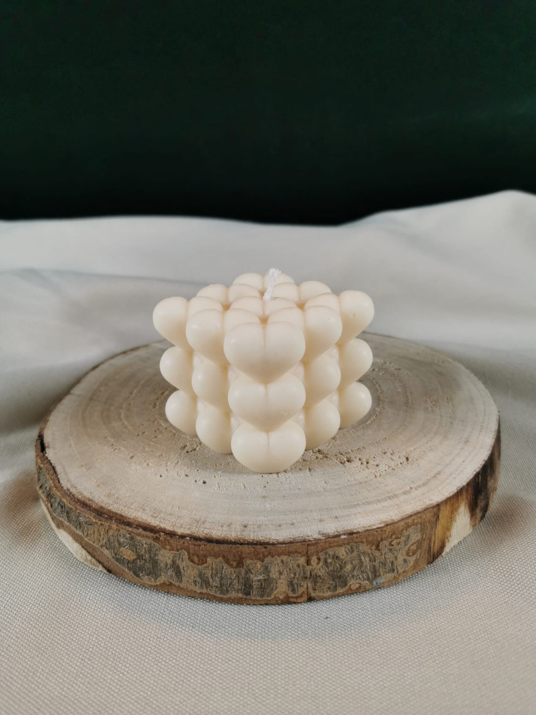 Handgegossene Bubble-Kerze aus hellem Rapswachs, bestehend aus vielen kleinen Wachskugeln, dekorativ auf einer Holzscheibe platziert.