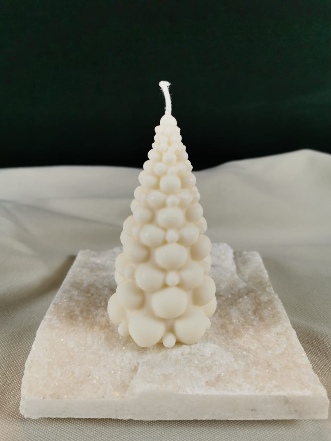 Handgegossene Bubble-Tannenbaum-Kerze aus hellem Bio-Rapswachs, dekorativ auf einer glitzernden Steinplatte präsentiert.