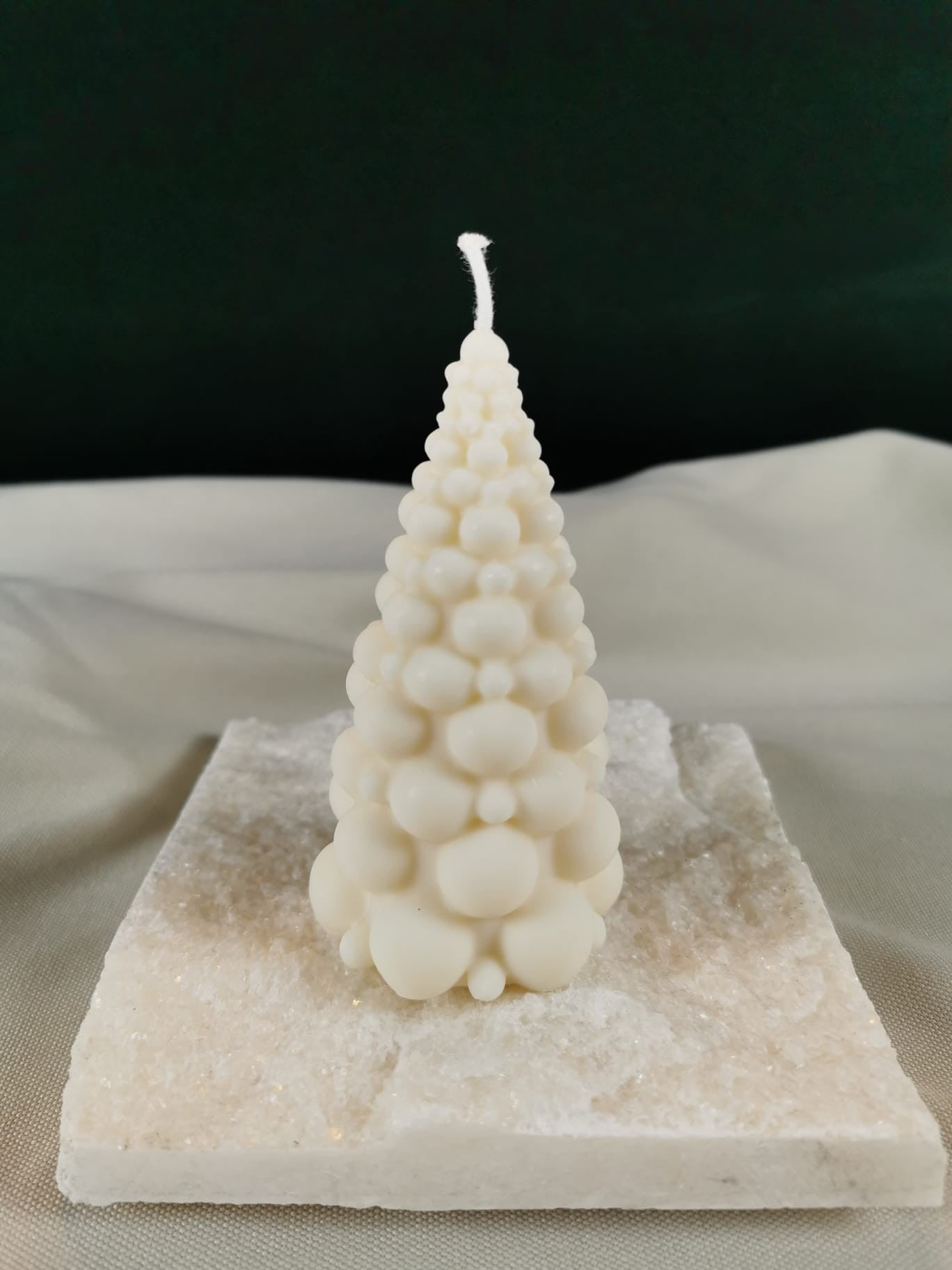 Handgegossene Bubble-Tannenbaum-Kerze aus hellem Bio-Rapswachs, dekorativ auf einer glitzernden Steinplatte präsentiert.