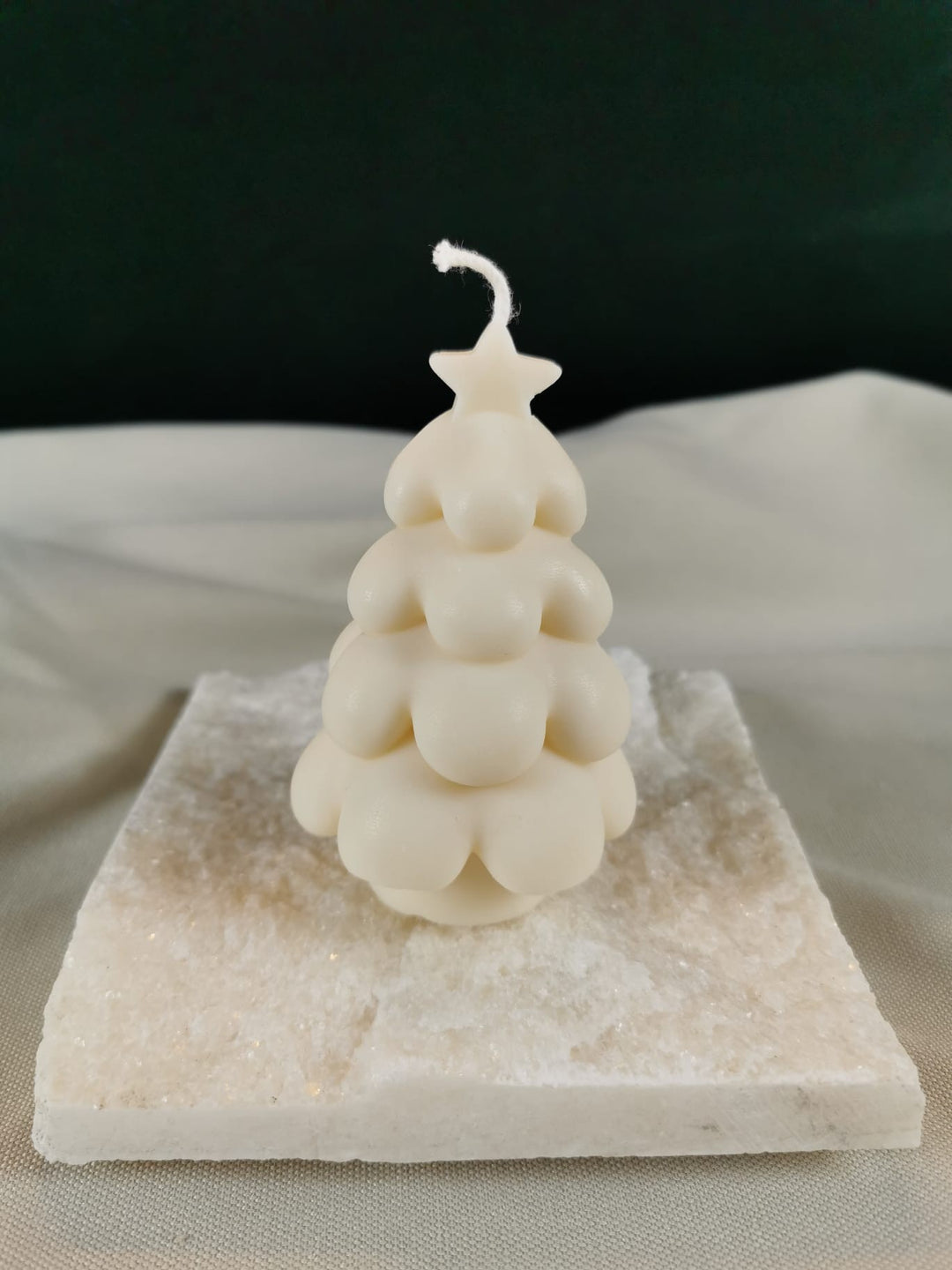 Handgegossene Tannenbaum-Kerze aus hellem Rapswachs im Bubble-Design mit Stern an der Spitze, dekorativ auf einer hellen Steinplatte präsentiert.