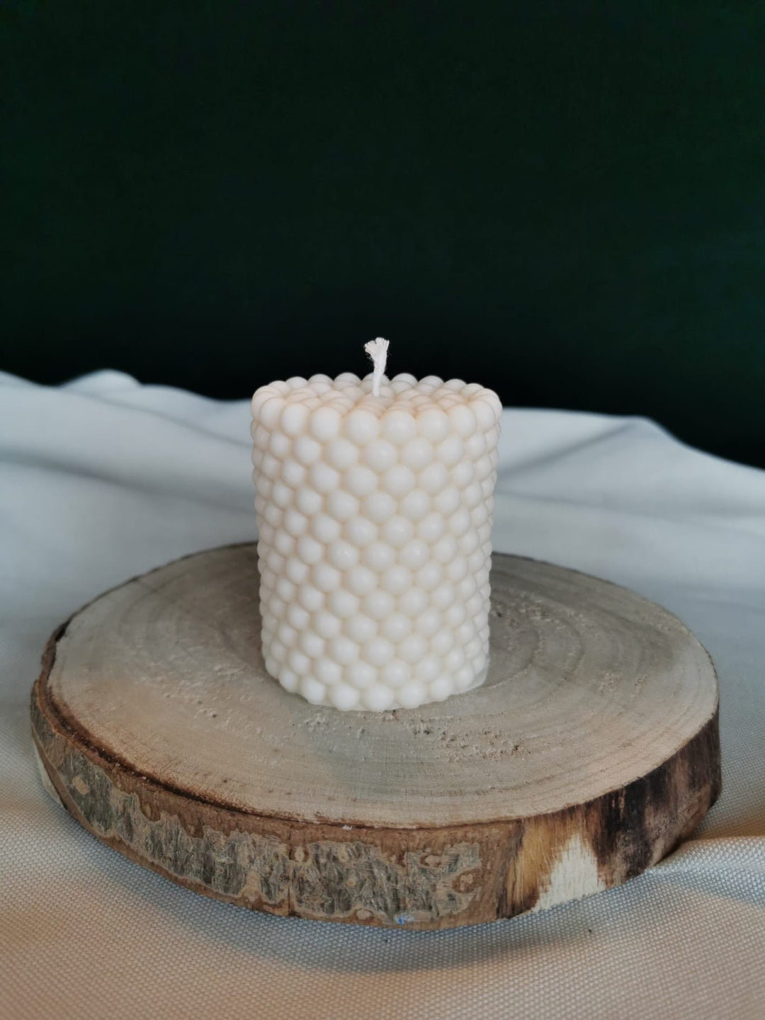 Handgegossene Bubble Zylinderkerze aus nachhaltigem Rapswachs auf Holzuntergrund – dekorative Kugelstruktur in Cremeweiß.