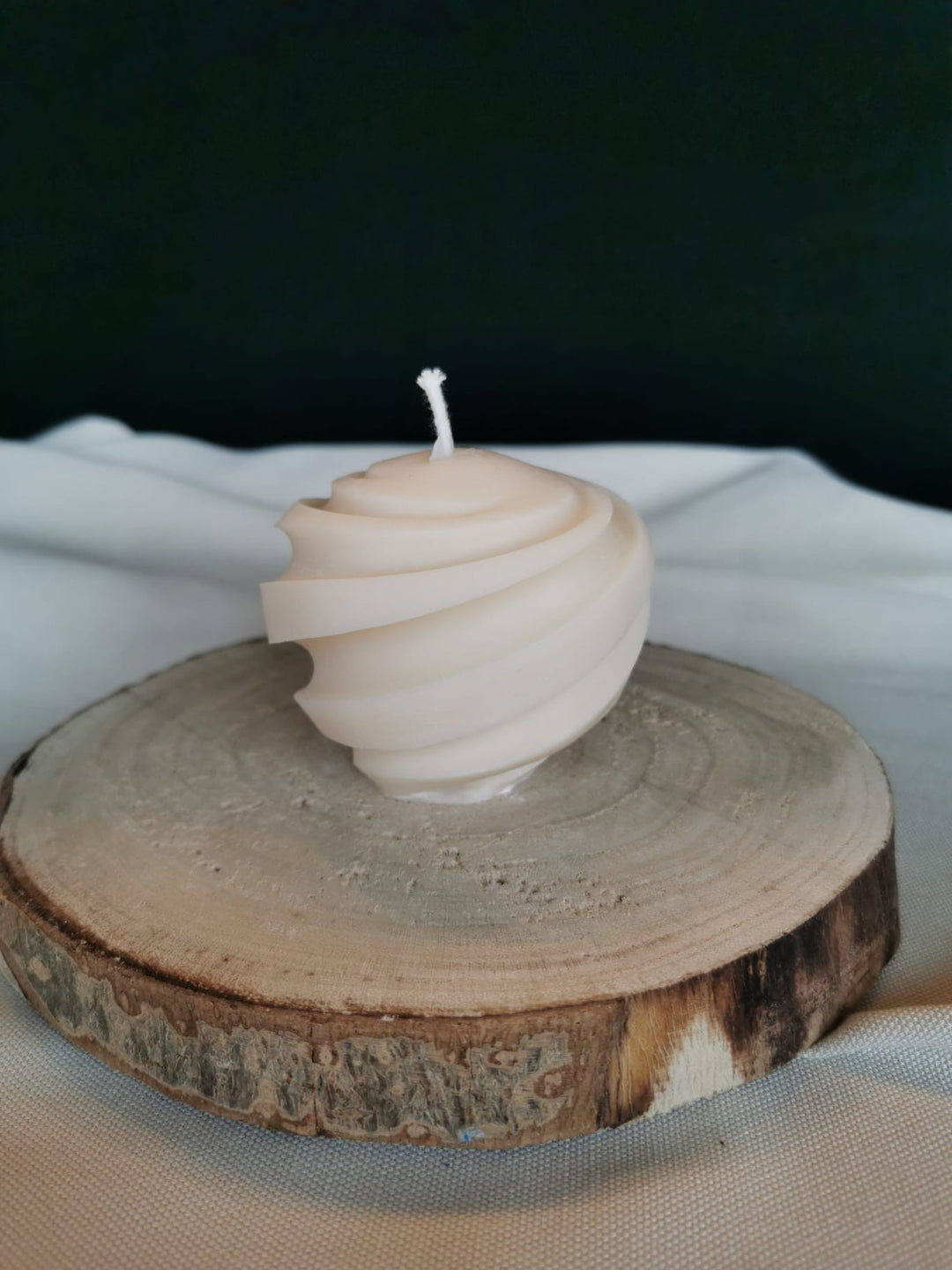Handgegossene Spiral-Designkerze aus natürlichem Rapswachs, dekorativ präsentiert auf einer Holzscheibe.
