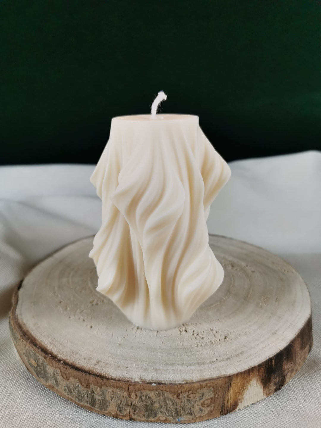 „Handgegossene dekorative Rapswachskerze in fließender Drapier-Optik auf Holzunterlage – elegante skulpturale Kerze in Creme.“