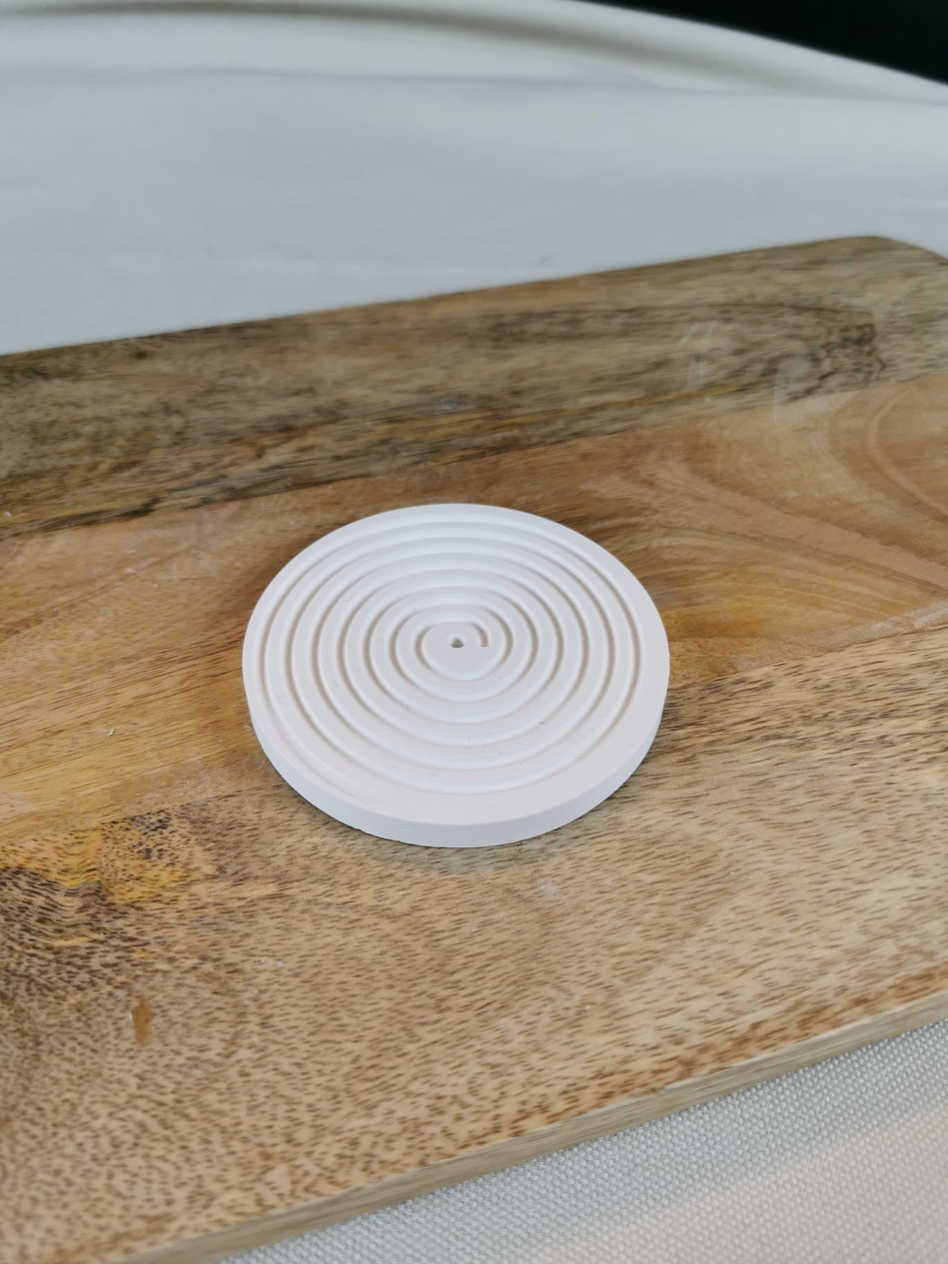 „Weißer Duftstein mit konzentrischen Kreisen und Räucherstäbchenhalter auf Holzuntergrund.“
