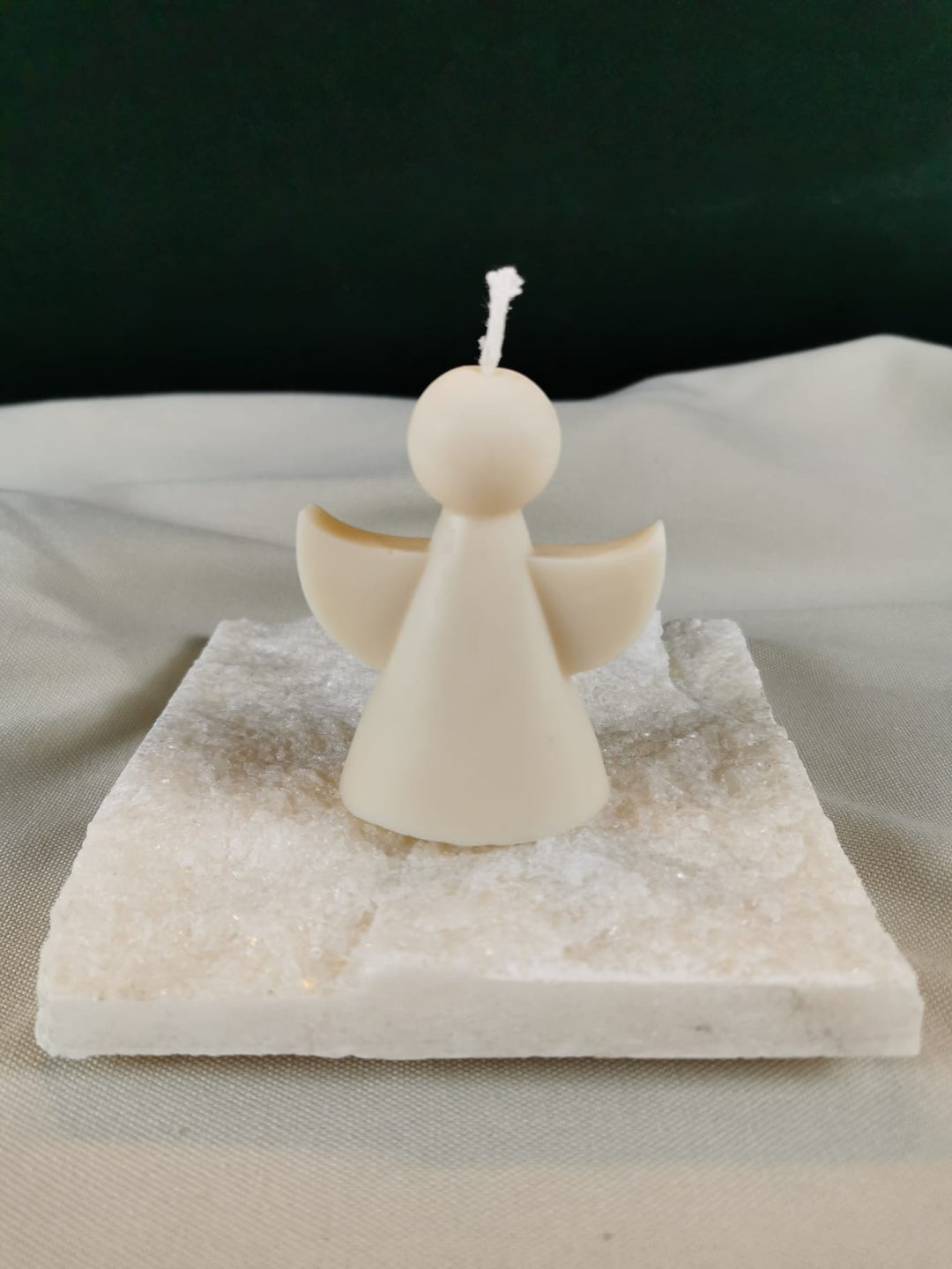 Handgegossene Engel-Figurenkerze aus hellem Rapswachs mit ausgebreiteten Flügeln, auf einer hellen Steinplatte präsentiert.