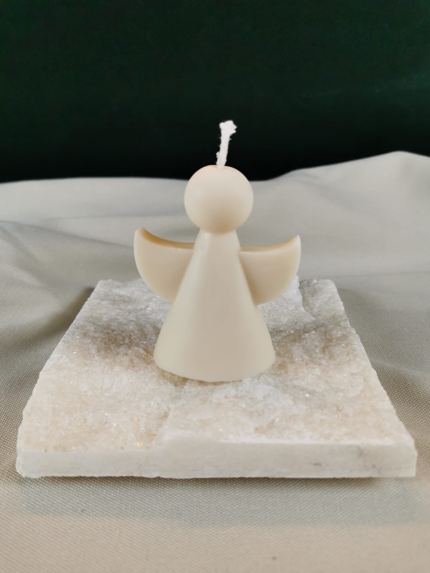 Handgegossene Engel-Figurenkerze aus hellem Rapswachs mit ausgebreiteten Flügeln, auf einer hellen Steinplatte präsentiert.