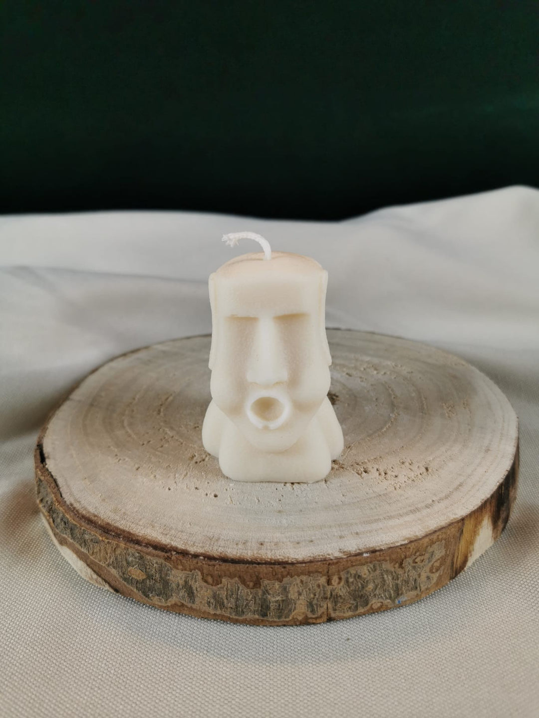 Handgegossene Figurenkerze aus hellem Rapswachs, die wie eine kleine stilisierte Steinfigur gestaltet ist. Die Kerze steht auf einer Holzscheibe vor einem sanften Hintergrund.