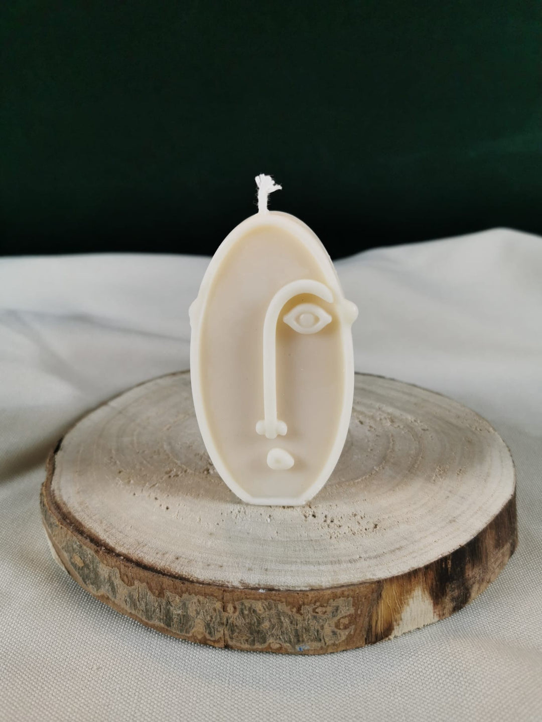 Handgegossene ovale Figurenkerze aus hellem Rapswachs mit abstrakter Gesichtslinie, dekorativ auf einer Holzscheibe präsentiert.