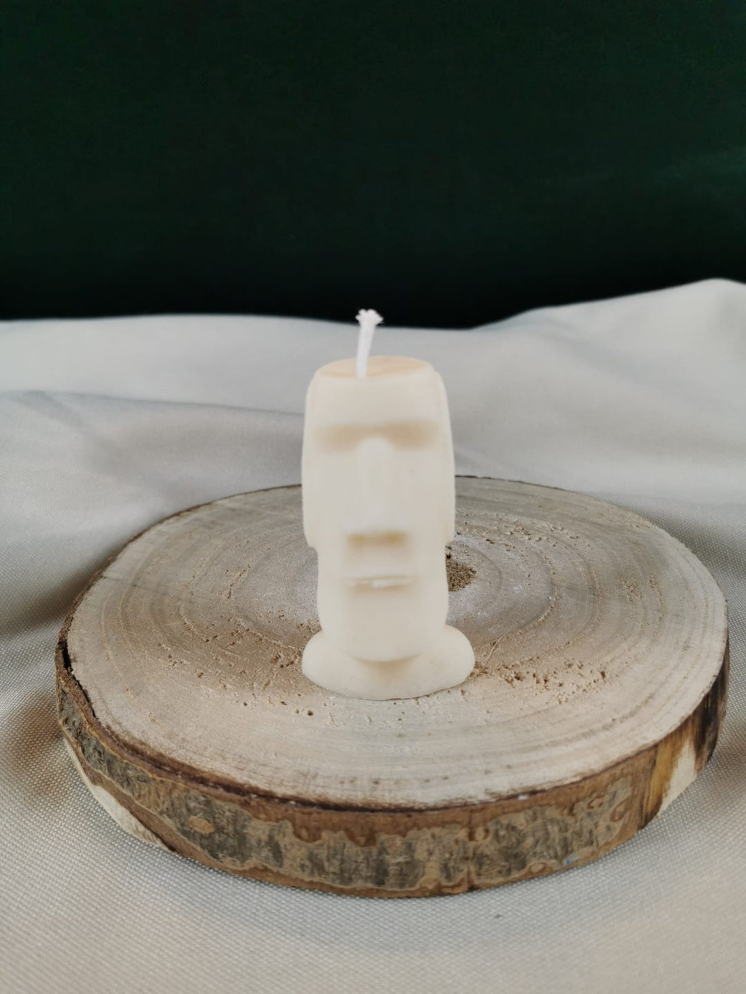 Handgegossene Figurenkerze aus hellem Rapswachs in Form eines schlichten, länglichen Kopfes, stehend auf einer runden Holzscheibe vor ruhigem Hintergrund.