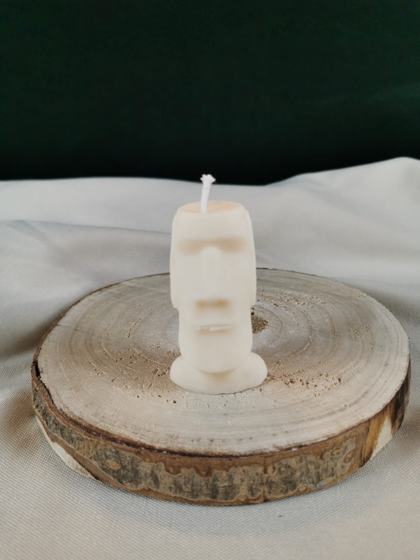 Handgegossene Figurenkerze aus hellem Rapswachs in Form eines schlichten, länglichen Kopfes, stehend auf einer runden Holzscheibe vor ruhigem Hintergrund.