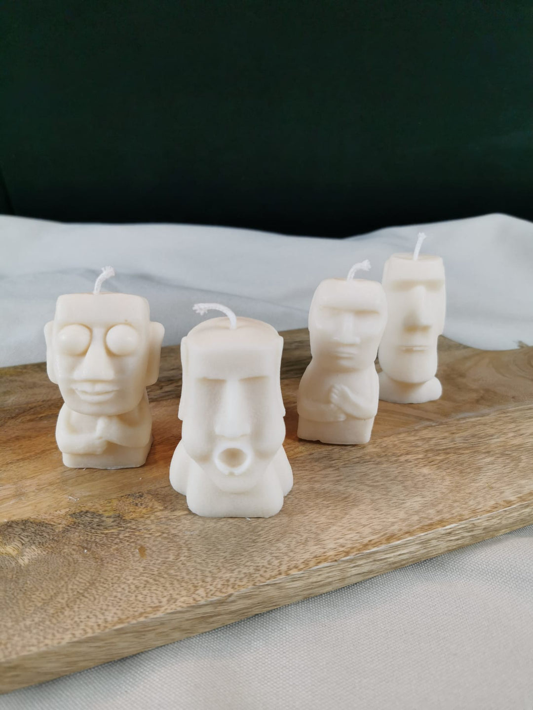 Vier handgegossene Figurenkerzen aus hellem Rapswachs, jede mit einer einzigartigen Gesichtsgestaltung, dekorativ auf einem Holzbrett arrangiert