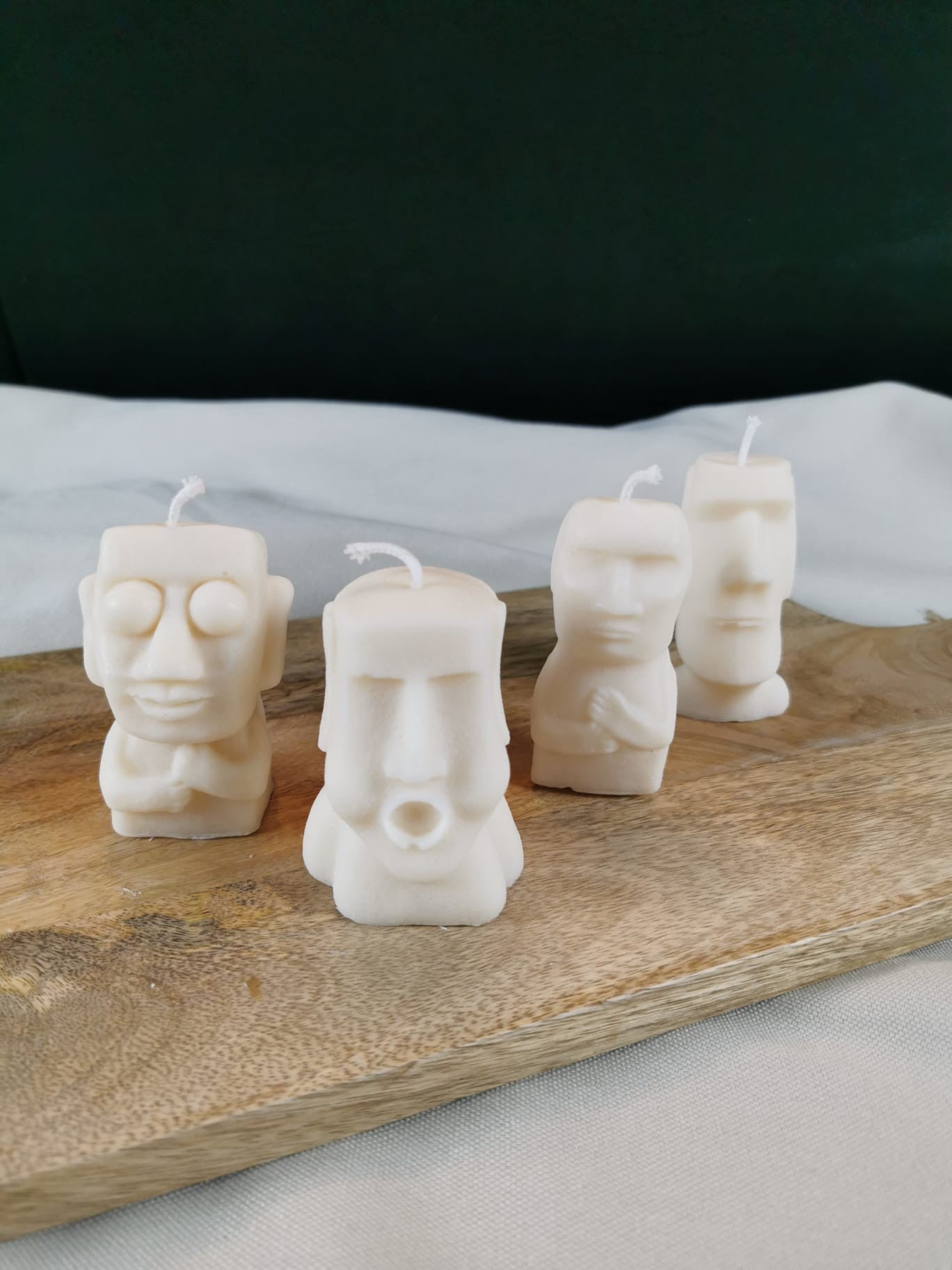 Vier handgegossene Figurenkerzen aus hellem Rapswachs, jede mit einer einzigartigen Gesichtsgestaltung, dekorativ auf einem Holzbrett arrangiert