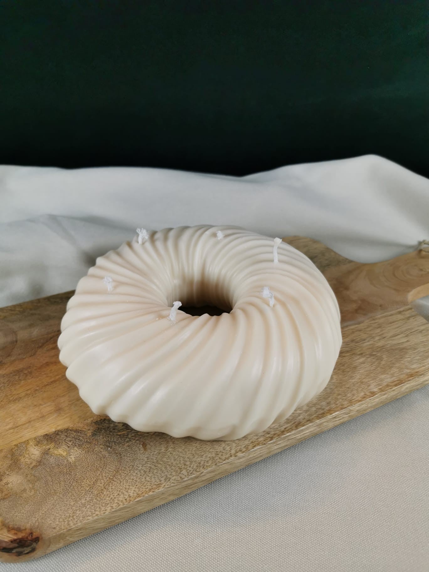 „Handgegossene gedrehte Ringkerze aus Rapswachs in Cremeweiß auf Holzunterlage.“