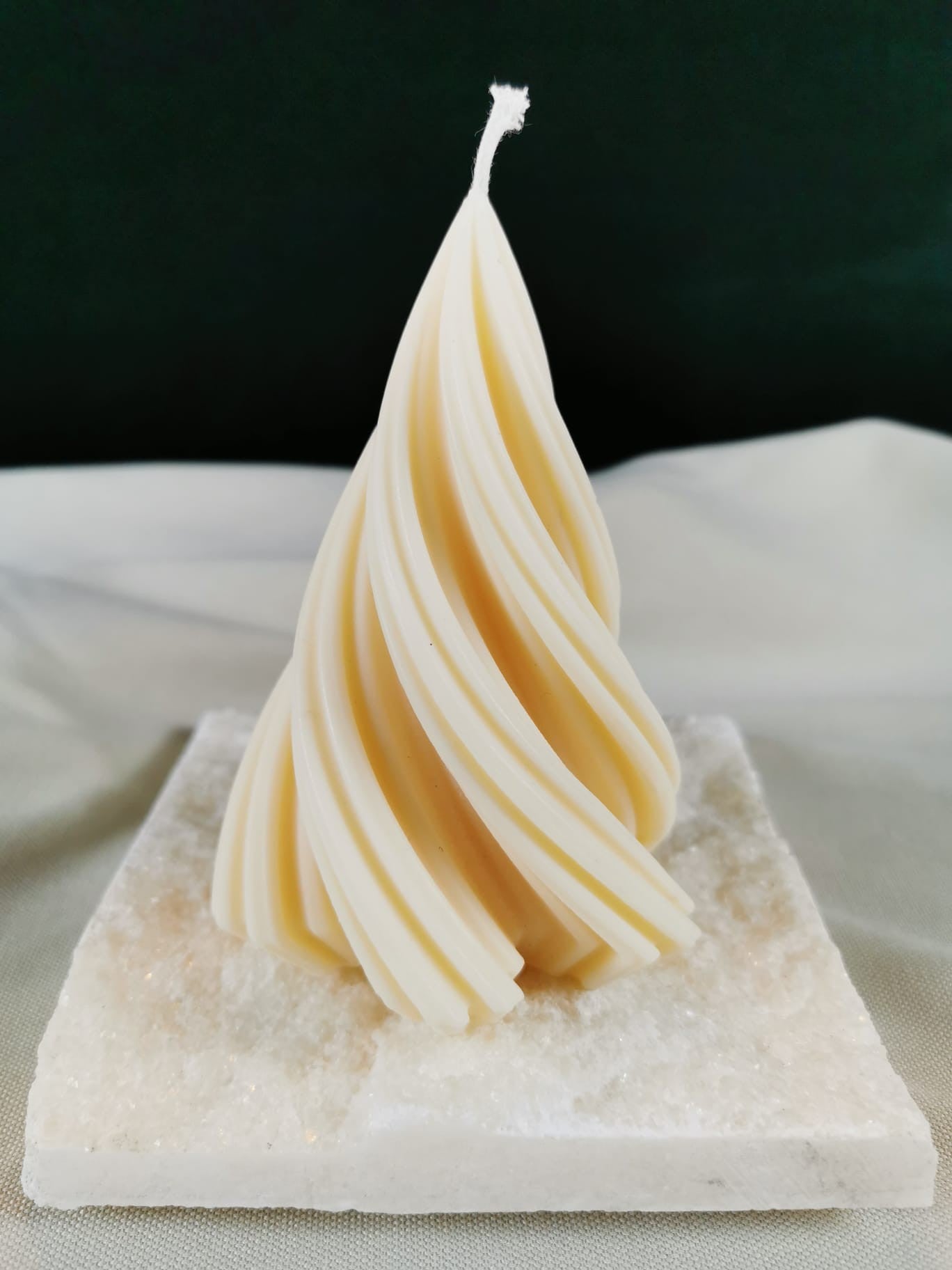 Handgegossene gedrehte Weihnachtsbaum-Kerze aus hellem Rapswachs auf glitzernder Steinplatte.