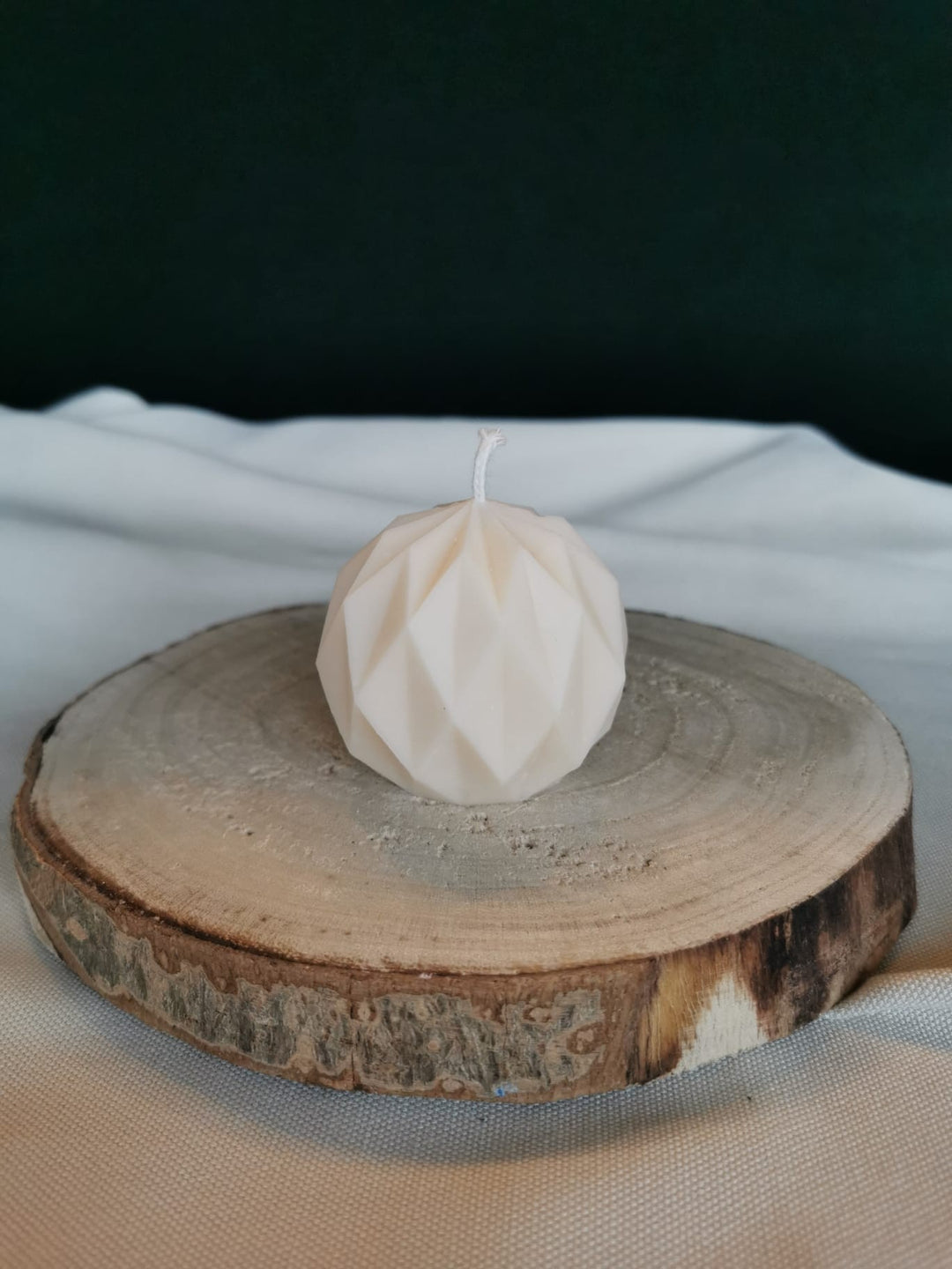 Weiße geometrische Kugelkerze aus Rapswachs mit facettierter Oberfläche, dekorativ auf einer Holzscheibe präsentiert.