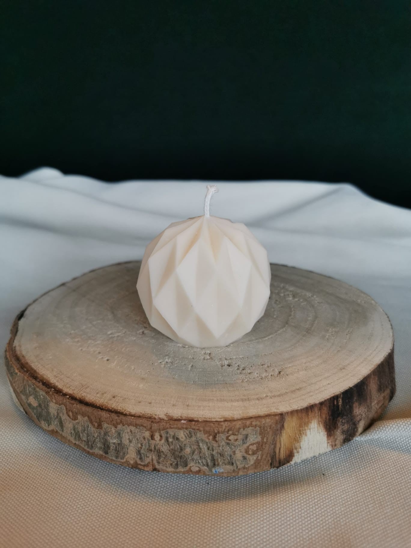 Weiße geometrische Kugelkerze aus Rapswachs mit facettierter Oberfläche, dekorativ auf einer Holzscheibe präsentiert.