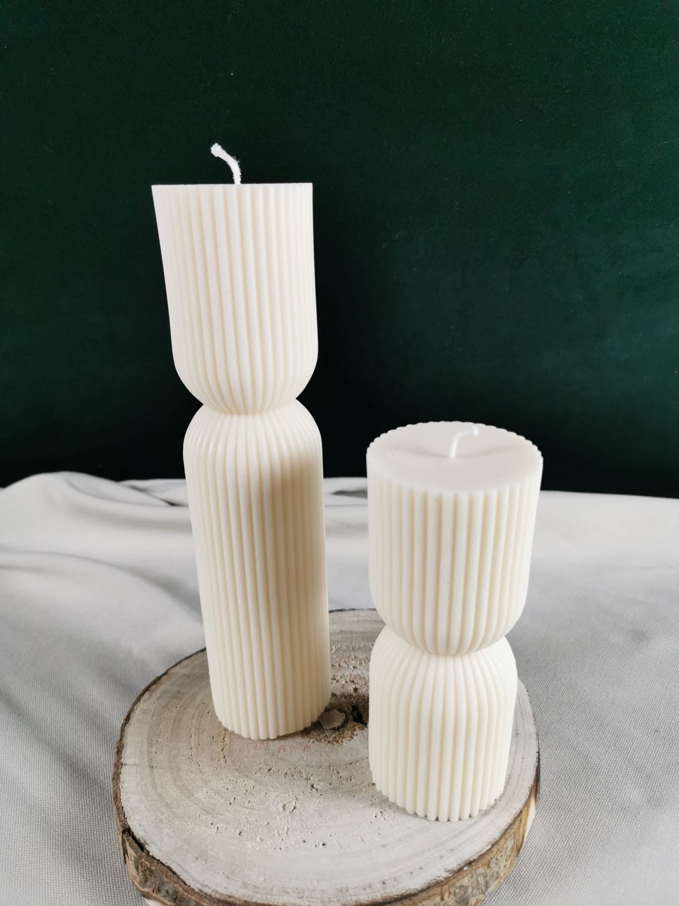 „Zwei handgegossene, cremefarbene Rapswachskerzen im modernen geriffelten Design, fotografiert auf einer Holzscheibe – große und kleine Version.“