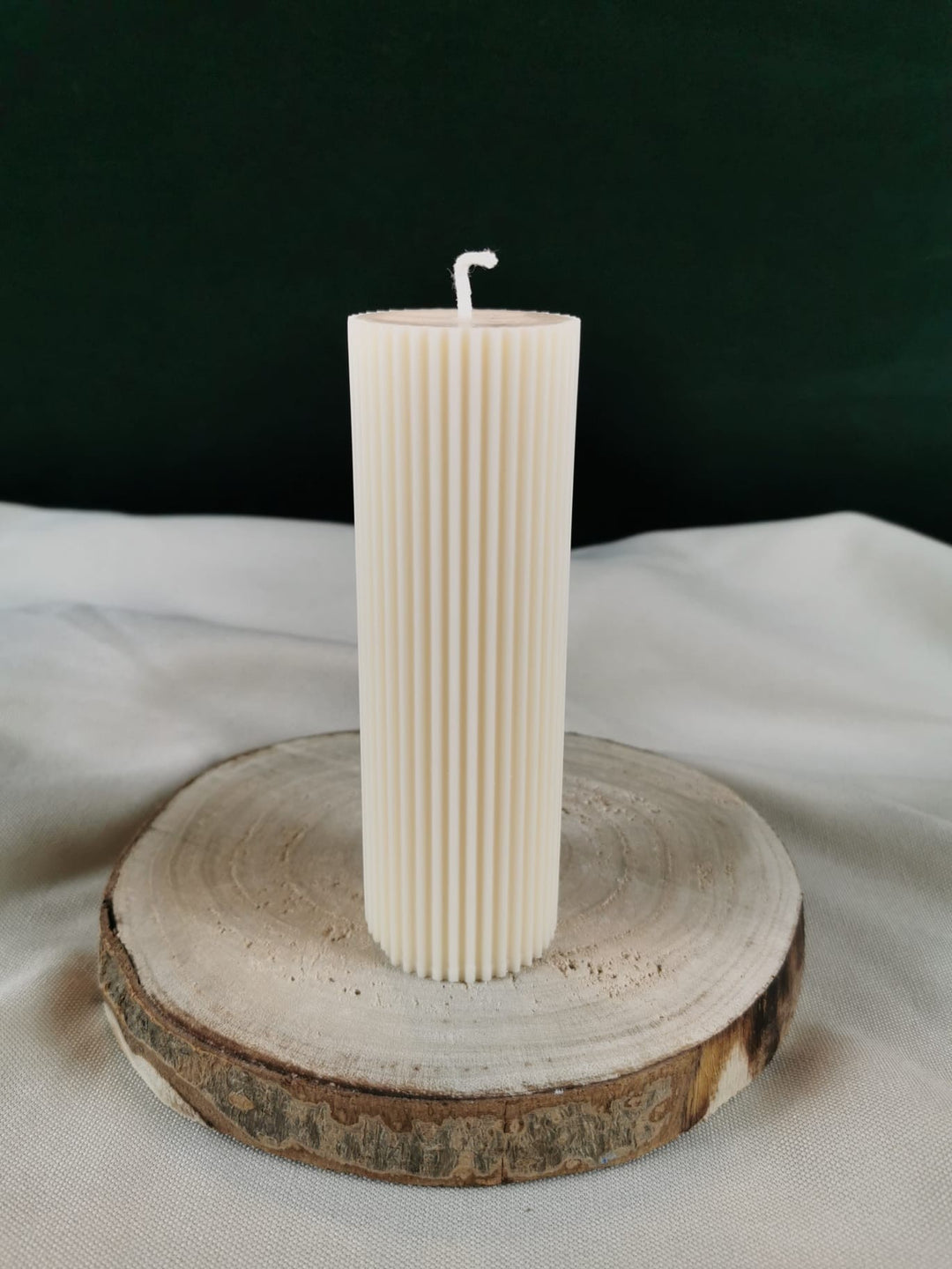„Handgegossene gerillte Stabkerze aus Rapswachs in Cremeweiß auf Holzuntergrund.“