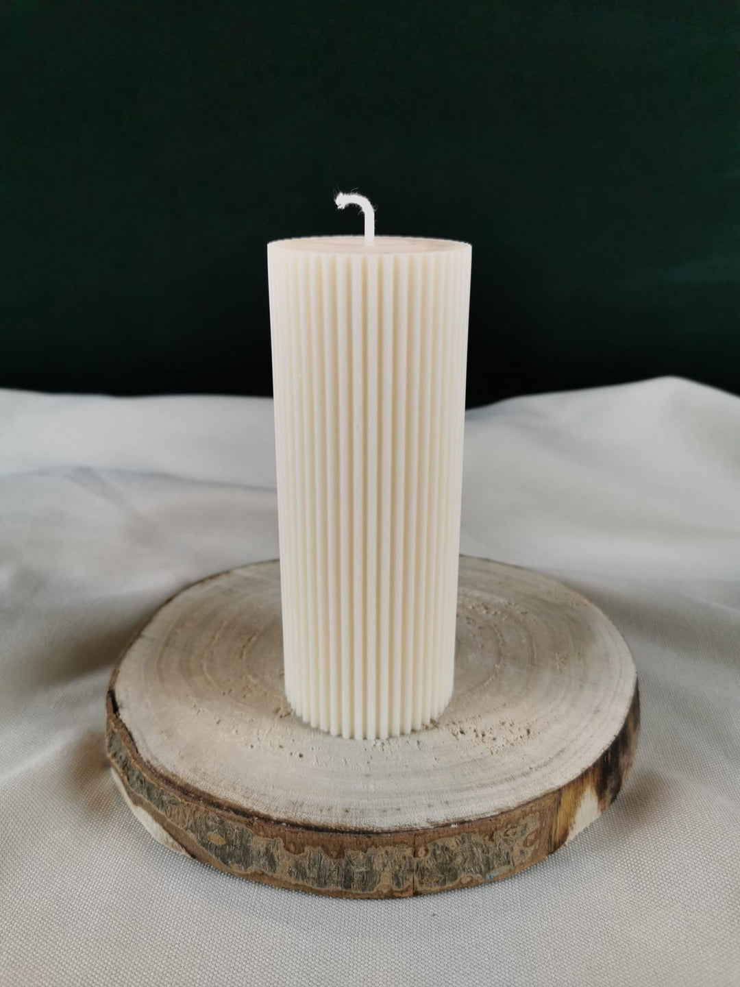 „Handgemachte gerillte Stumpenkerze aus Rapswachs in Cremeweiß auf Holzuntersetzer.“