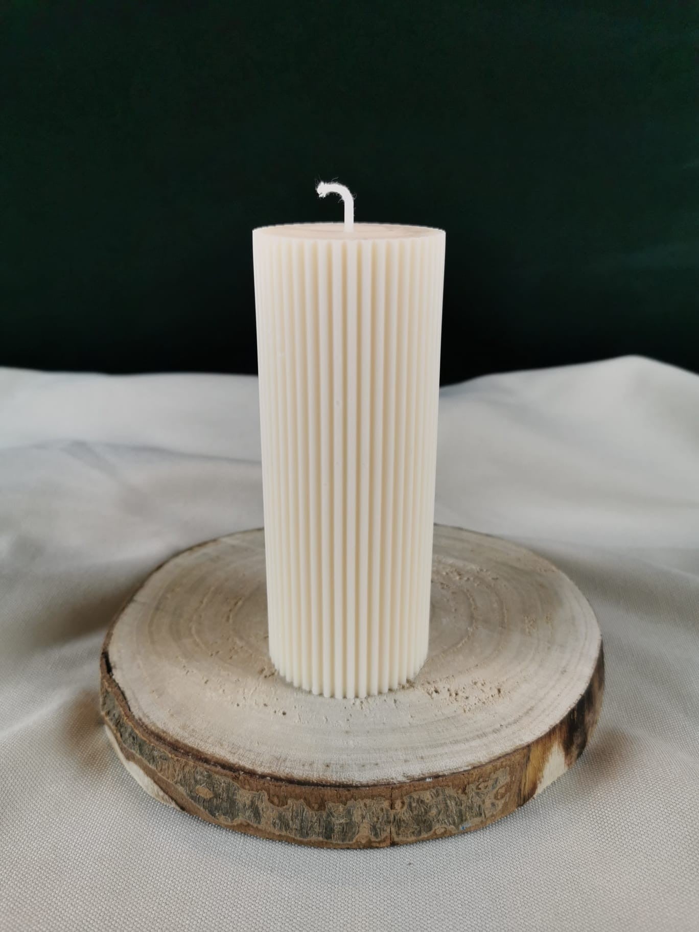 „Handgemachte gerillte Stumpenkerze aus Rapswachs in Cremeweiß auf Holzuntersetzer.“