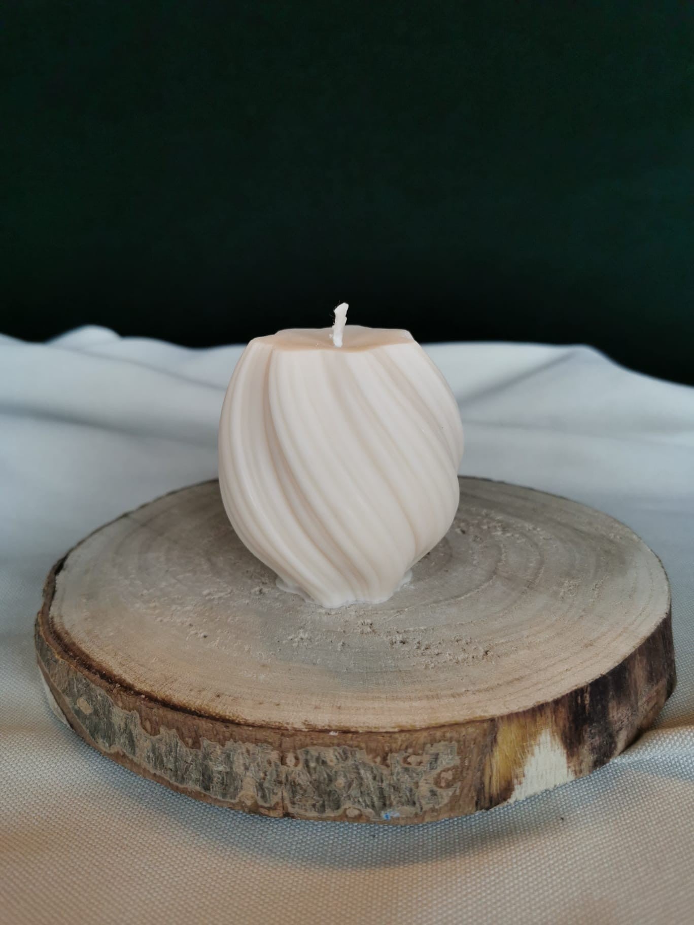 Geschwungene Mini-Skulpturkerze aus hellem Rapswachs, mit weichen, fließenden Linien, auf einem runden Holzbrett dekoriert.