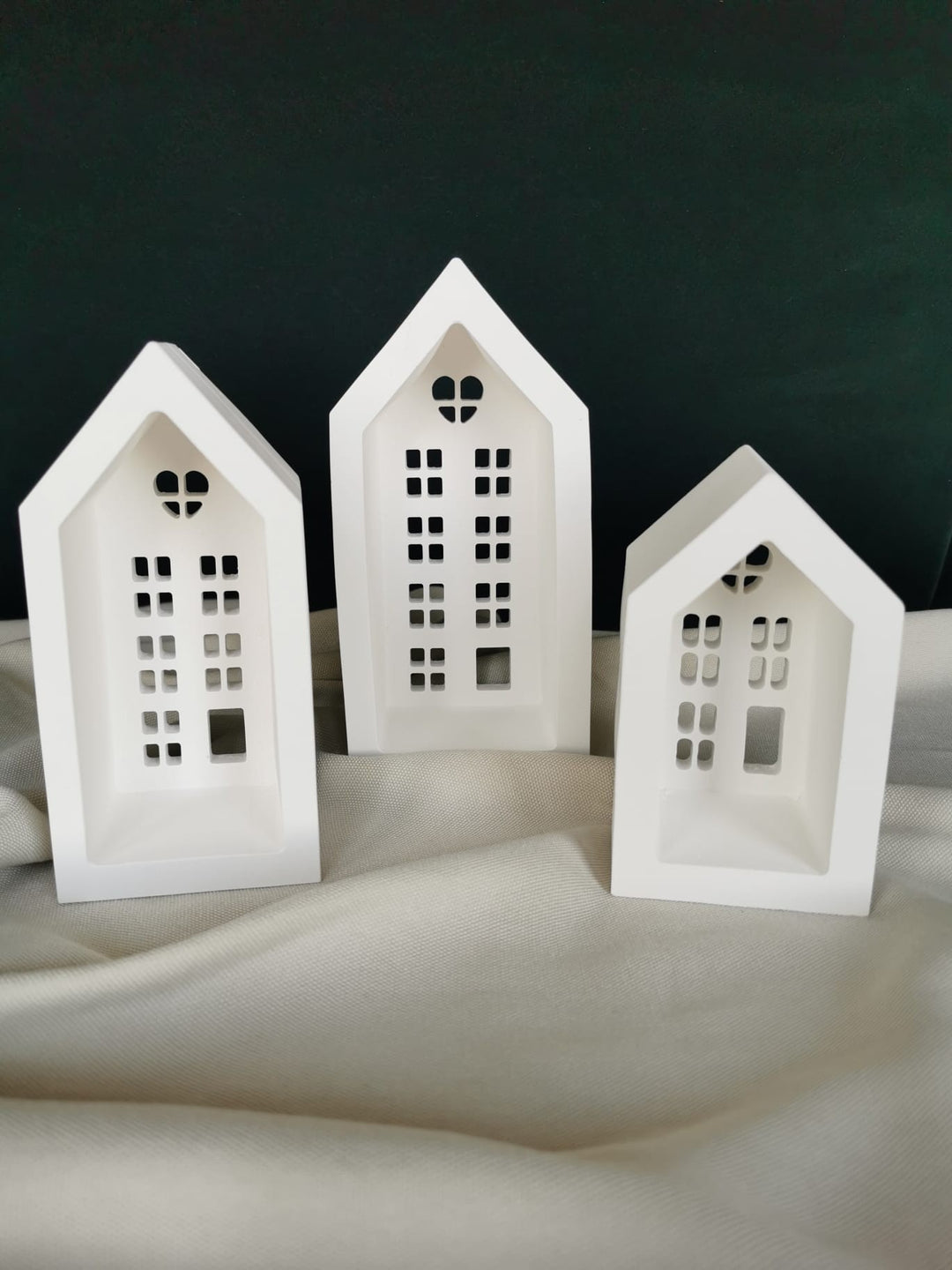 „Weiße Keramik-Lichthäuser im 3er-Set mit filigranen Fensteröffnungen – moderne Weihnachtsdeko auf Holztablett.“