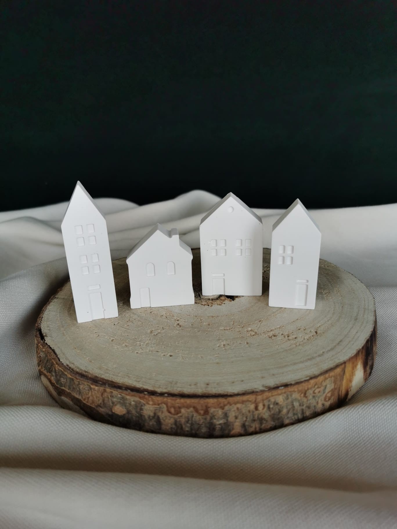 „Vier kleine weiße Keramik-Mini-Häuser als Winter- und Weihnachtsdeko auf einer Holzscheibe“