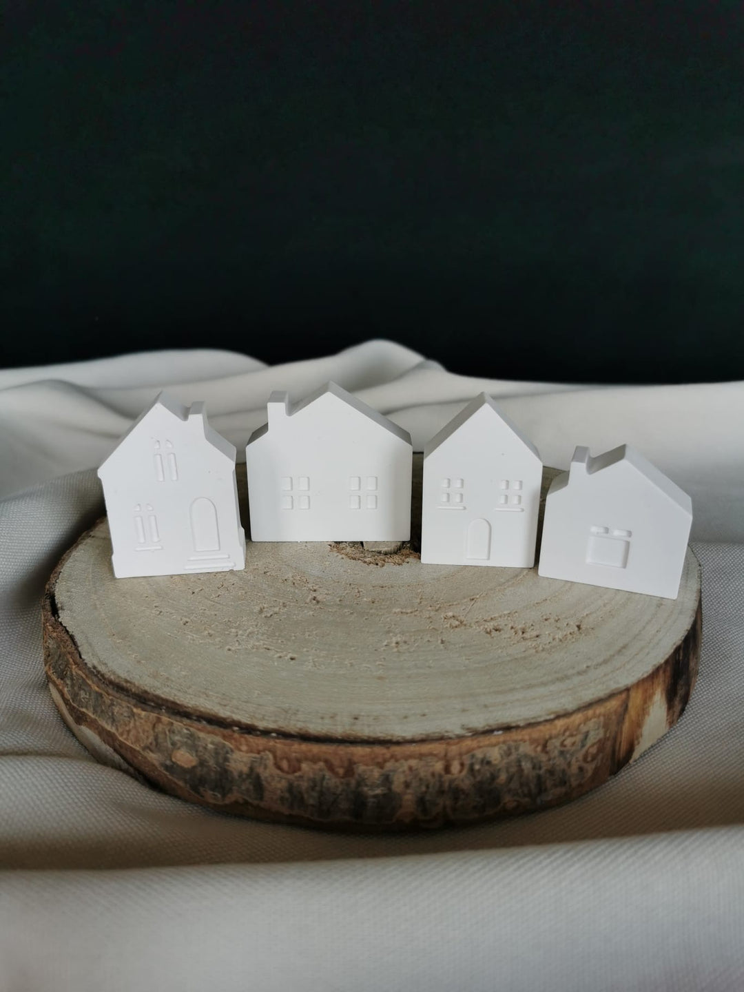 „Vier kleine weiße Keramik-Minihäuschen als Winterdorf-Deko auf Holzunterlage“