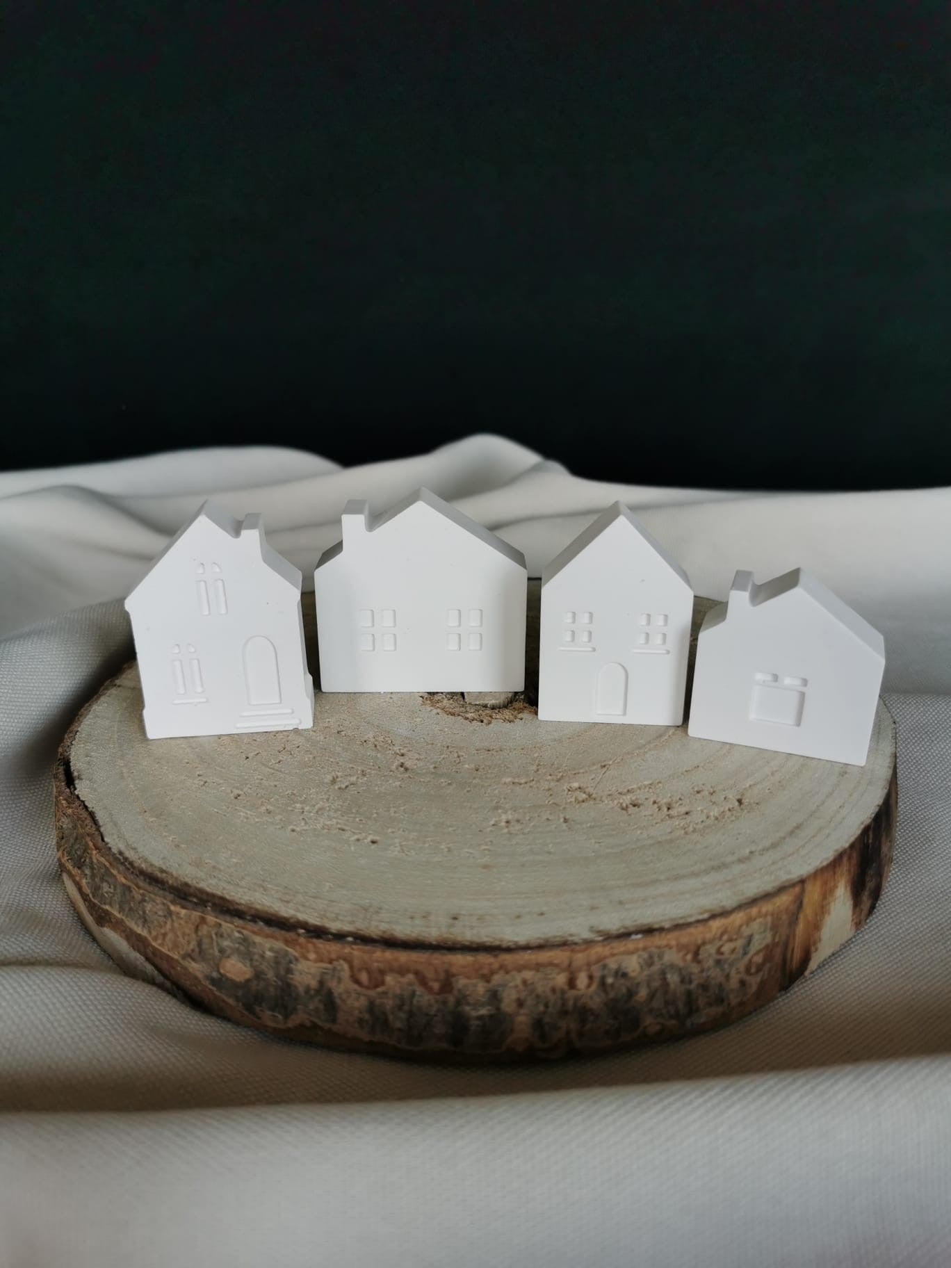 „Vier kleine weiße Keramik-Minihäuschen als Winterdorf-Deko auf Holzunterlage“