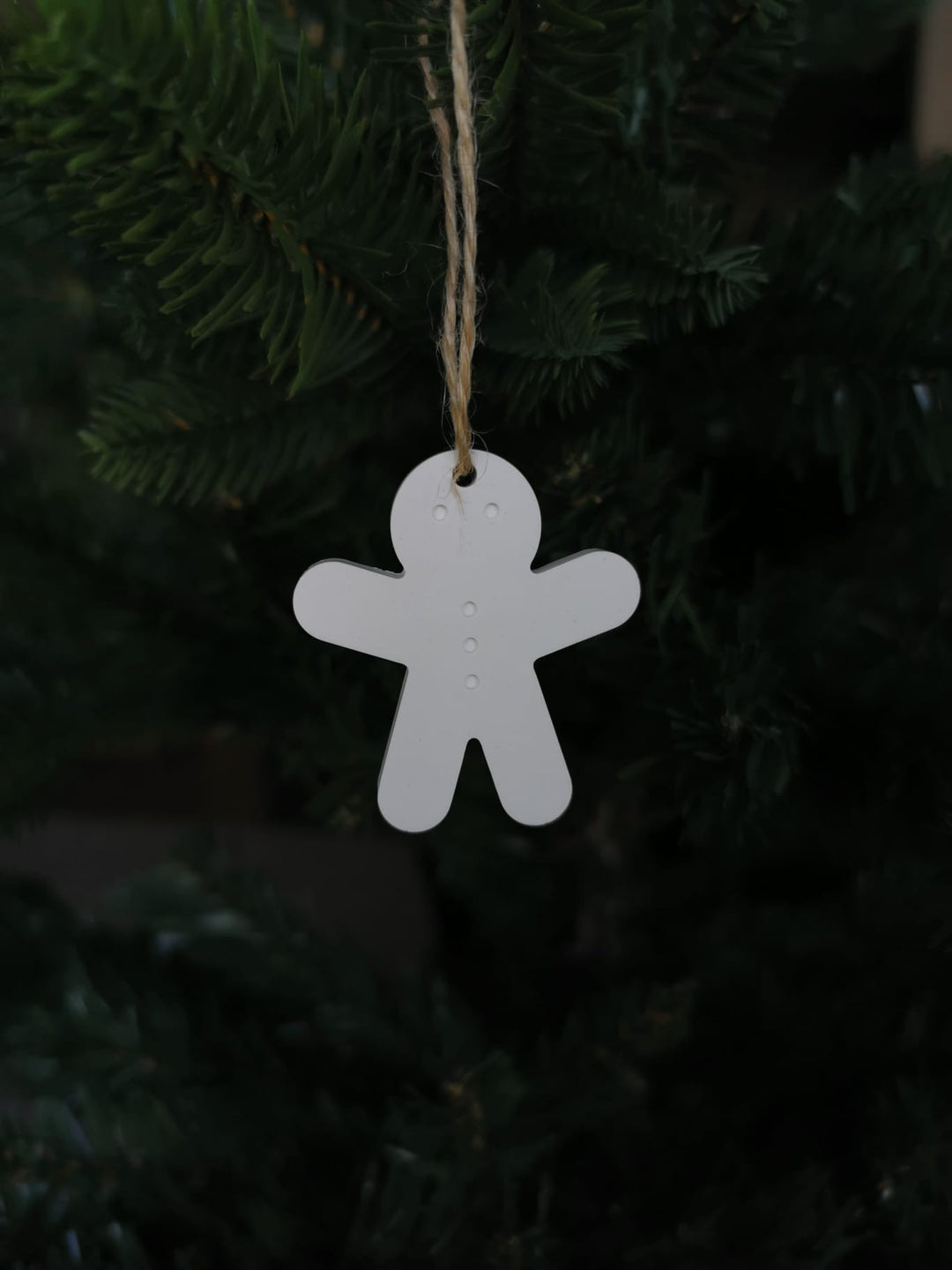 „Weißer Keramik-Lebkuchenmännchen-Anhänger mit Juteschnur an einem Tannenzweig.“