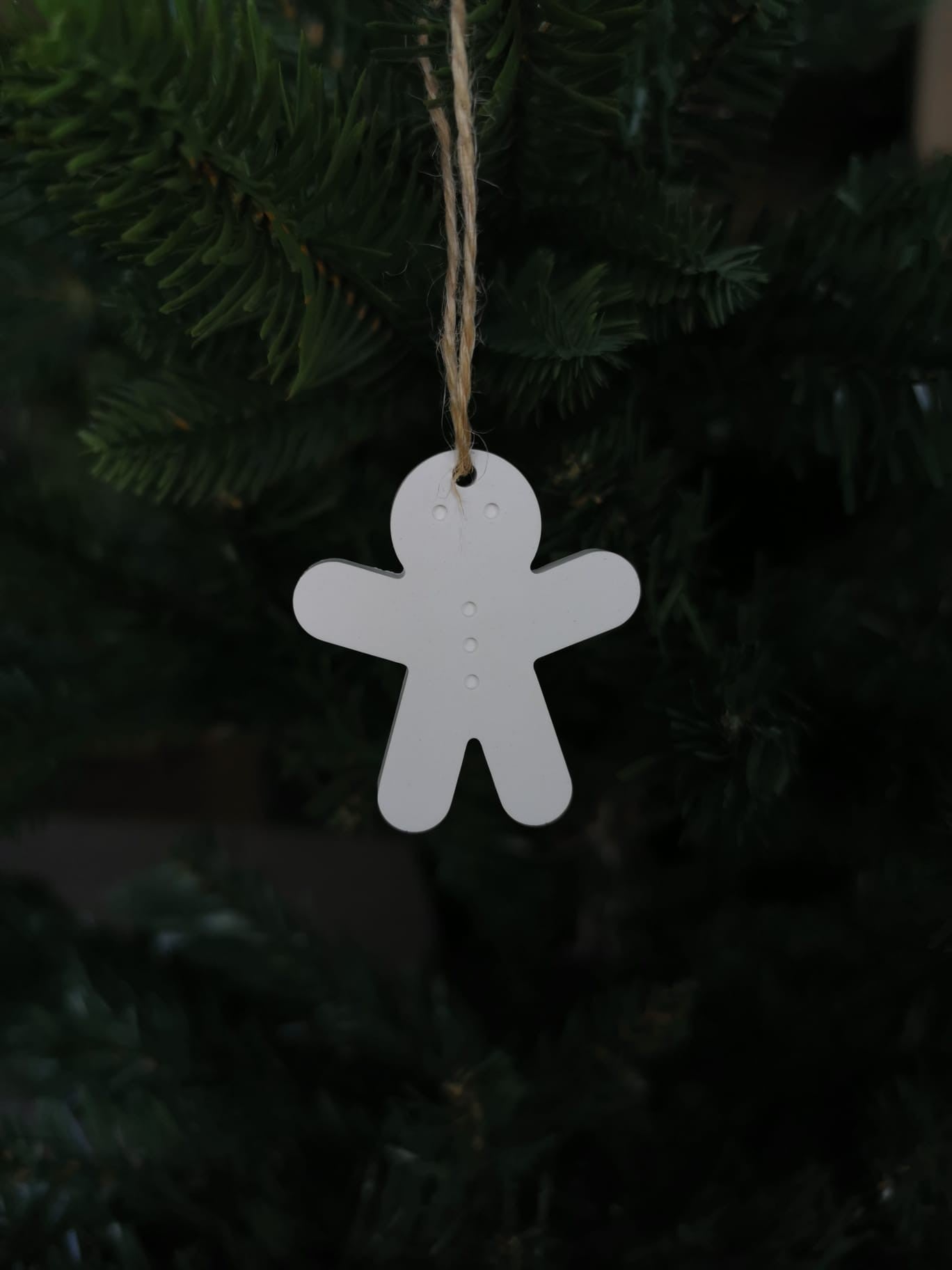 „Weißer Keramik-Lebkuchenmännchen-Anhänger mit Juteschnur an einem Tannenzweig.“