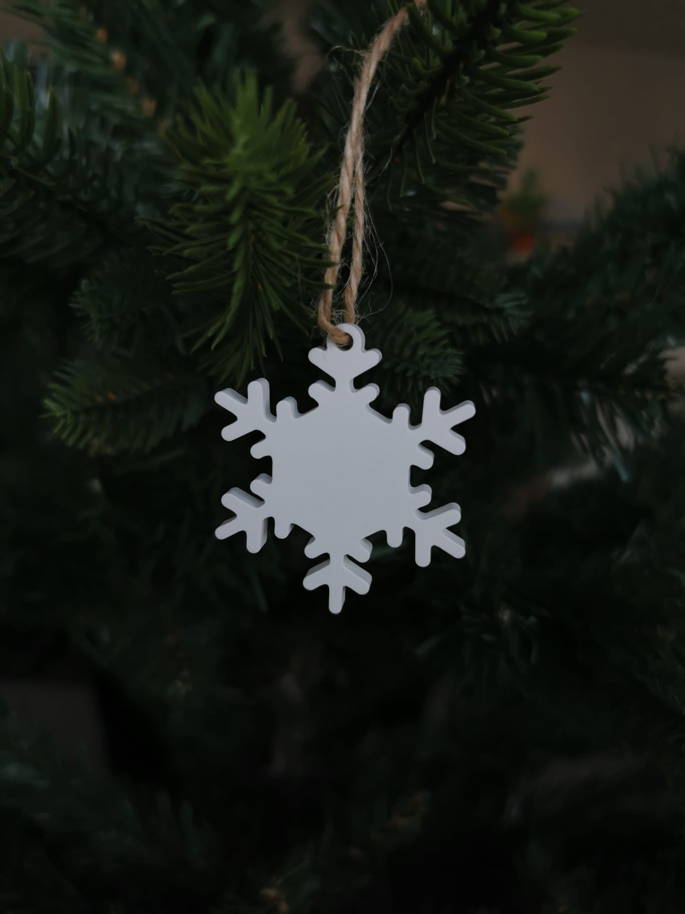 „Weiße Keramik-Schneeflocke mit Juteschnur an Tannenzweig.“