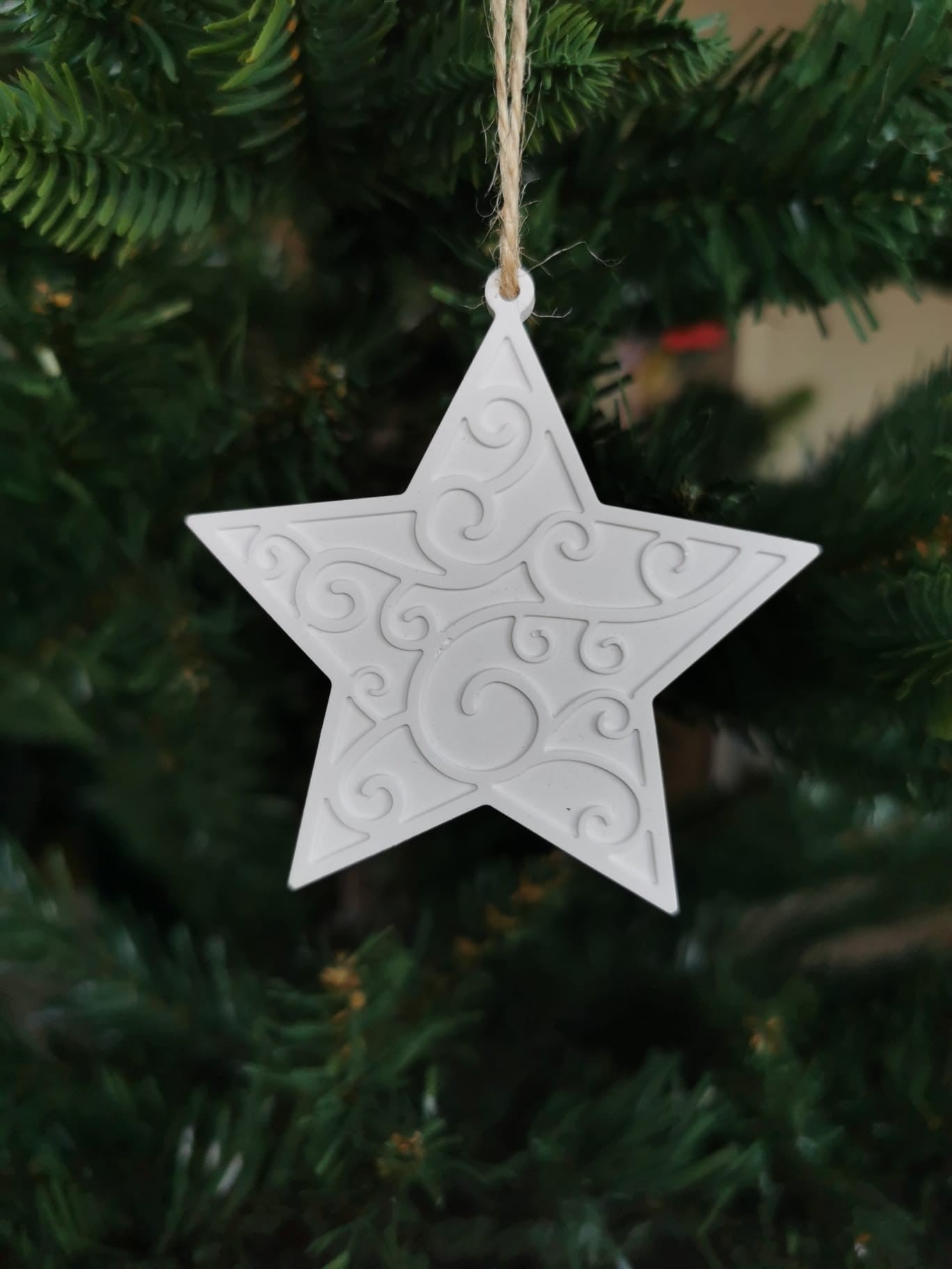„Weißer Keramikstern mit Ornament und Juteschnur an einem Tannenzweig.“