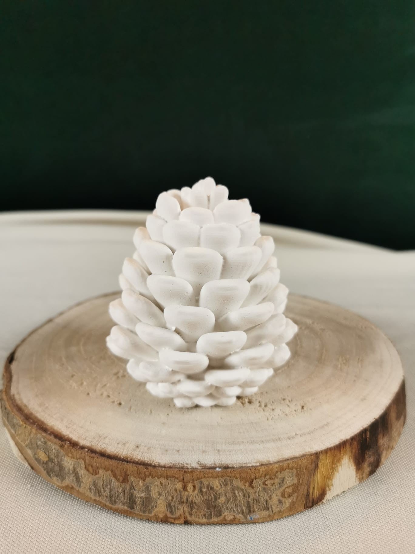 Weißer handgefertigter Keramik-Tannenzapfen auf Holzscheibe – dekorative Winter- und Weihnachtsdeko.