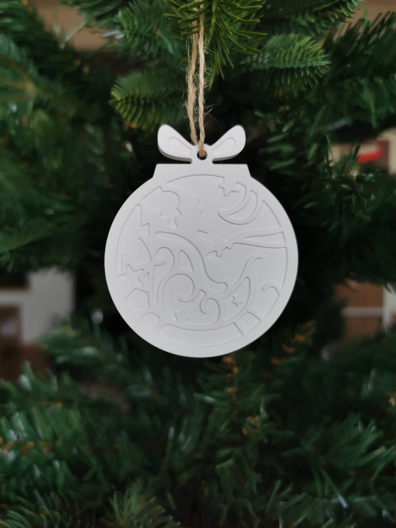 „Weißer Keramik-Baumanhänger in Kugelform mit Ornamentmuster, aufgehängt an einer Juteschnur im Weihnachtsbaum.“