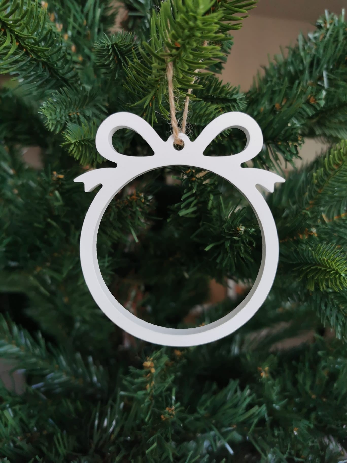 Weißer Keramik Weihnachtsanhänger in Form einer Schleife mit offenem Kreis, hängend am Weihnachtsbaum.
